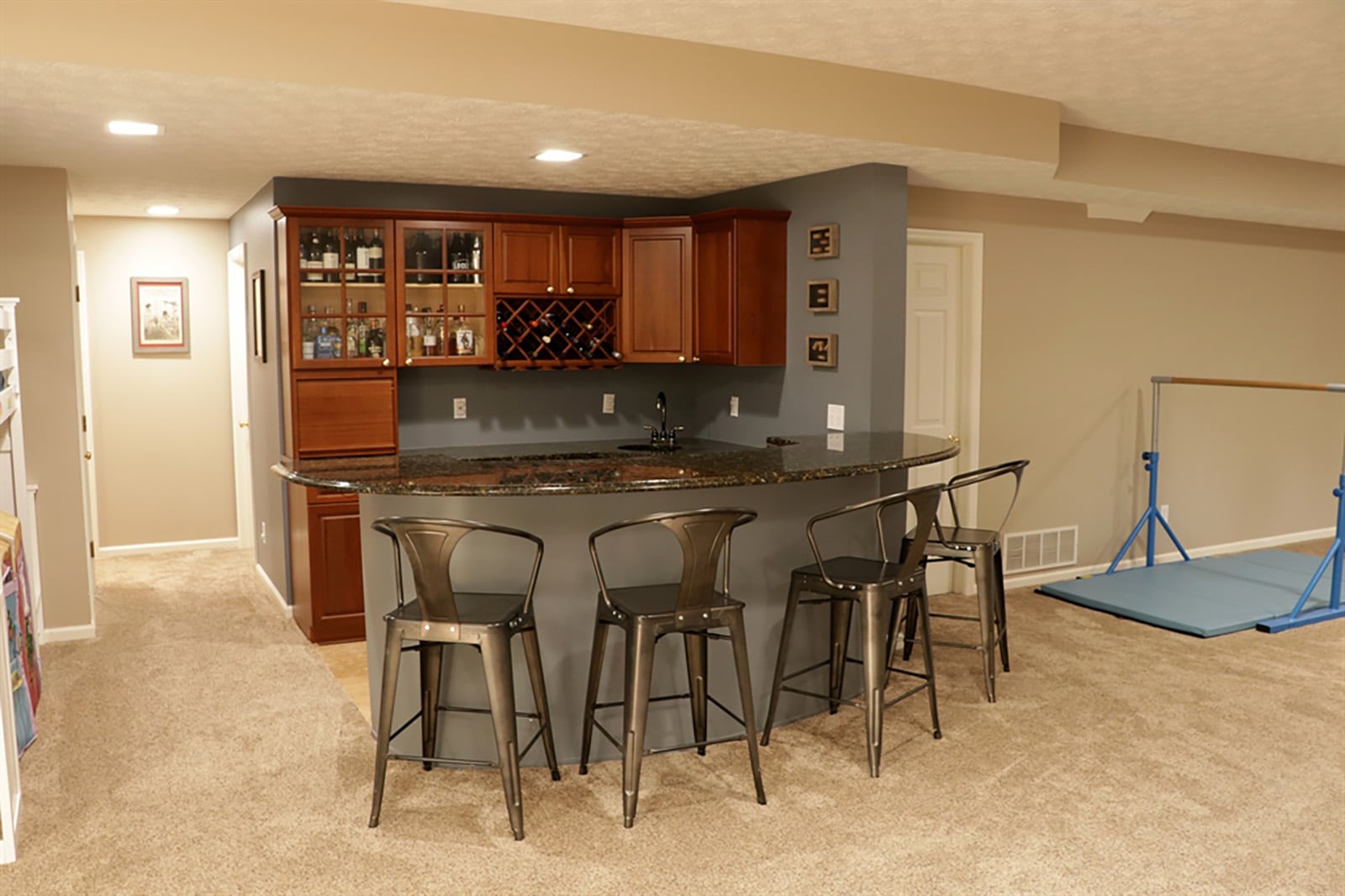 A peninsula bar in the walk-out lower level has a 2-level granite counter top and seating space for up to six. The wall space has hanging cabinetry that includes glass and bottle racks, and glass-front doors. CONTRIBUTED PHOTO BY KATHY TYLER