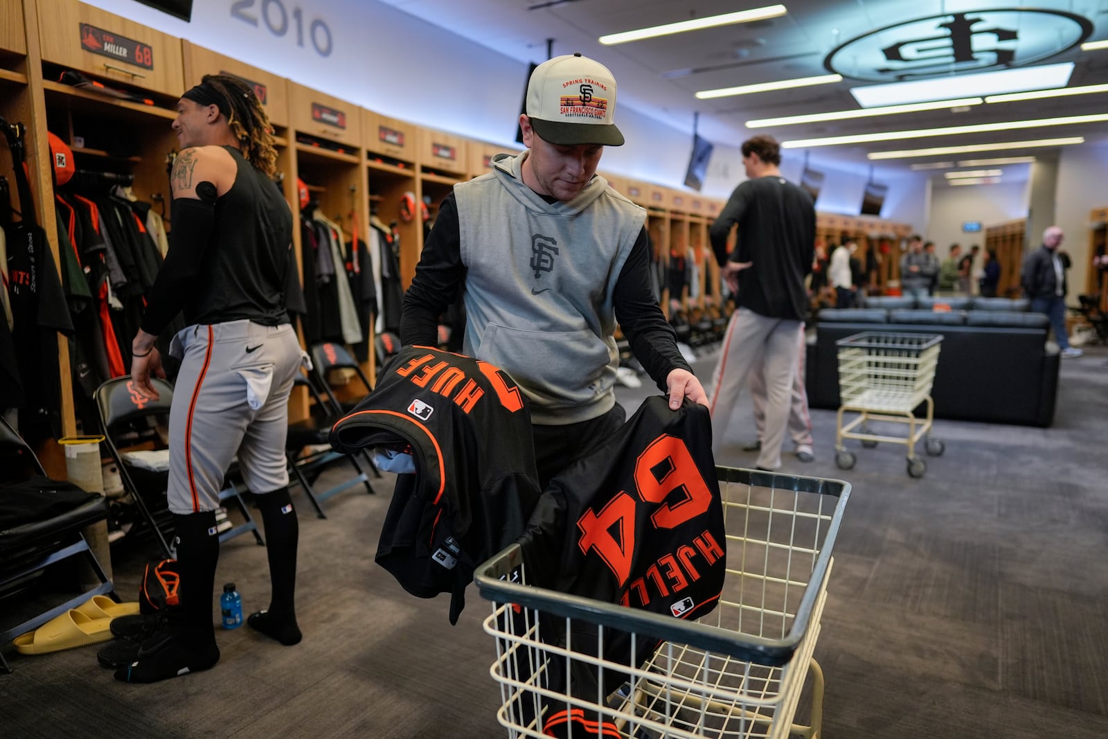 San Francisco Giants clubhouse attendant Riley Halpin gathers dirty clothes in the clubhouse after spring training baseball practice at the team's facility, Monday, Feb. 17, 2025, in Scottsdale, Ariz. (AP Photo/Carolyn Kaster)