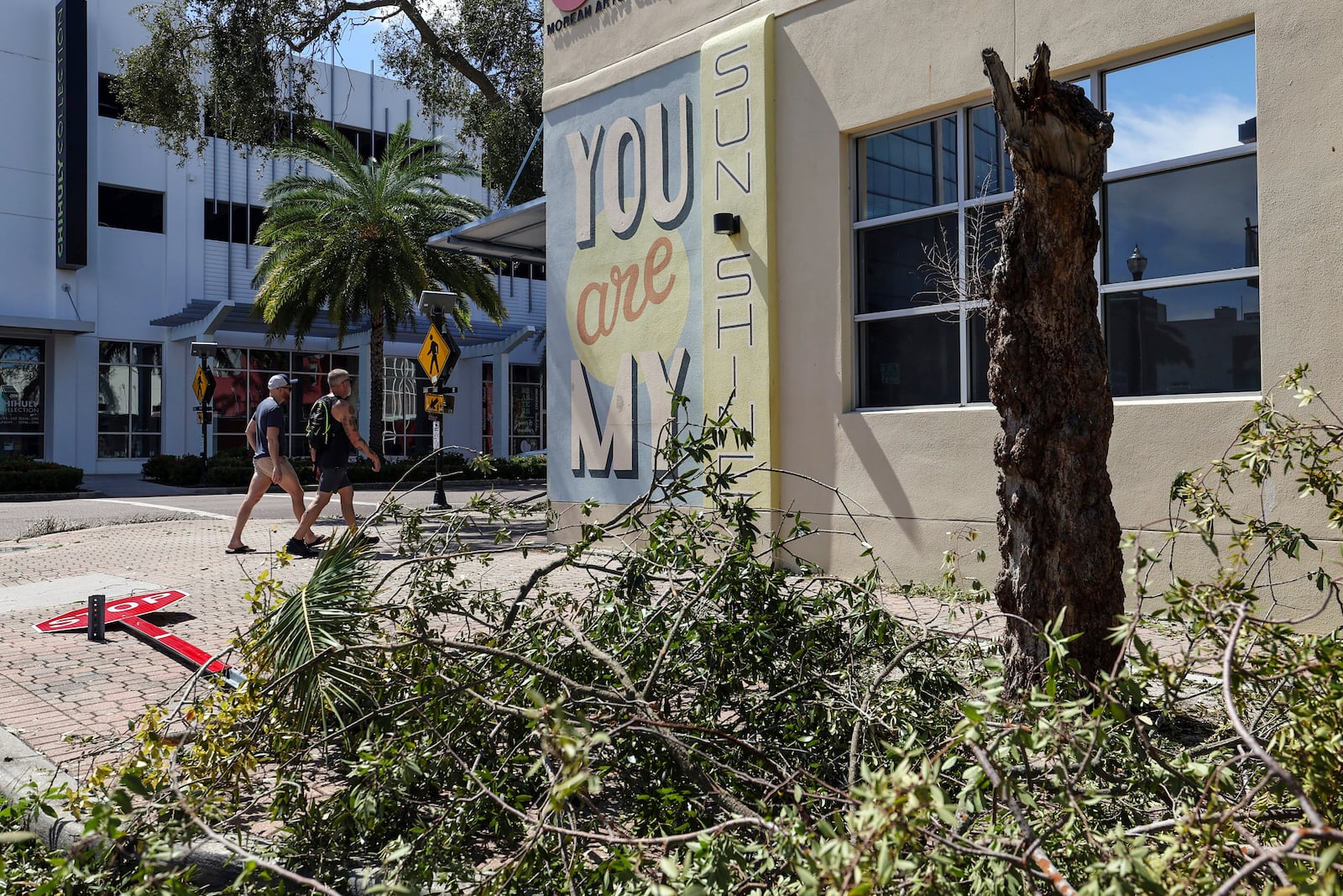 Residents walk past trees and signs damaged by winds from Hurricane Milton on Thursday, Oct. 10, 2024, in St. Petersburg, Fla. (AP Photo/Mike Carlson)