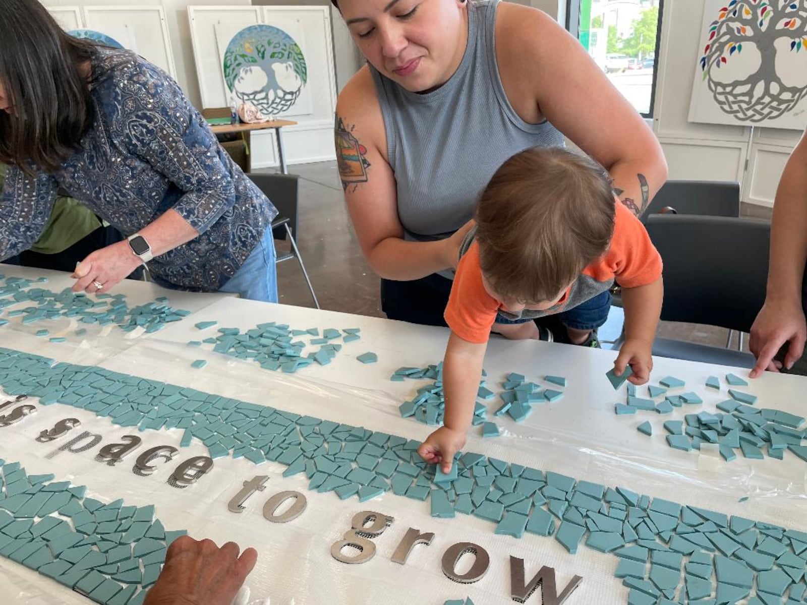 Yuri Pimentel holds 18-month-old Jaxson Childress as he places a tile on the 8/4 Memorial mosaic. PHOTO BY RUSSELL FLORENCE JR.