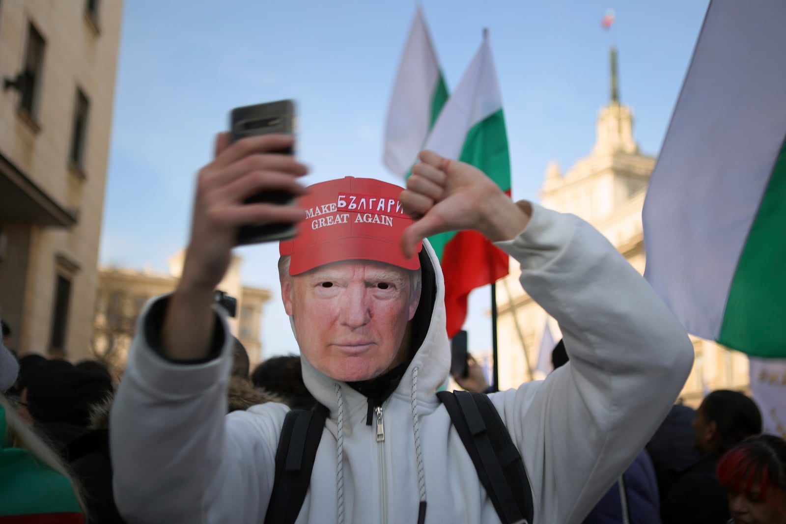 A protester wearing a mask of Donald Trump with a sign "Make Bulgaria strong again" shows thumb down during a protest demanding the government to scrap plans to take the country into the eurozone, Sofia, Saturday, Feb. 22, 2025. (AP Photo/Valentina Petrova)