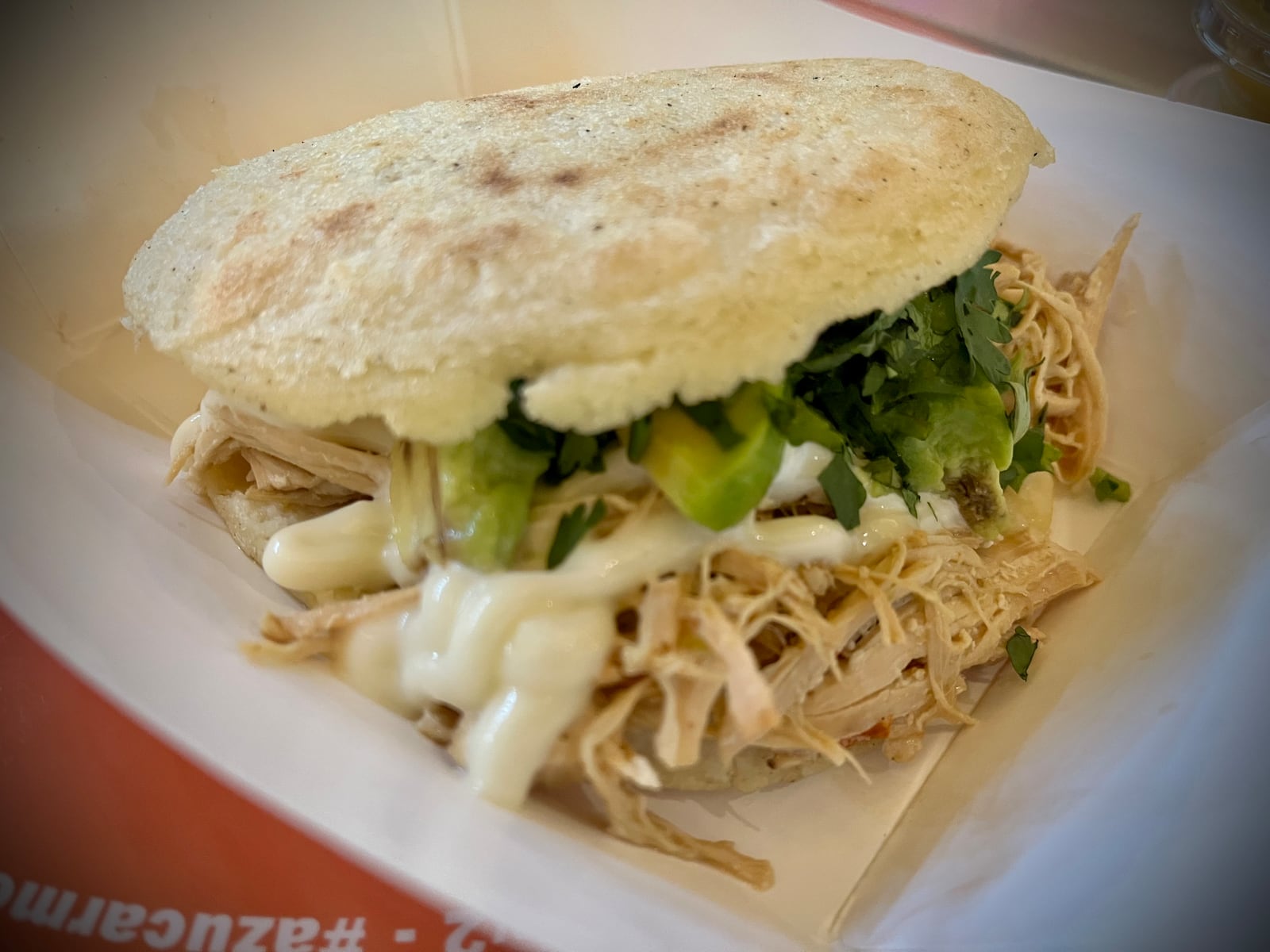 An arepa stuffed with shredded chicken, avocado, mayo and cilantro from Azucar Morena, a vendor inside The Garage Food Hall in Indiana that specializes in Venezuelan food. NATALIE JONES/STAFF