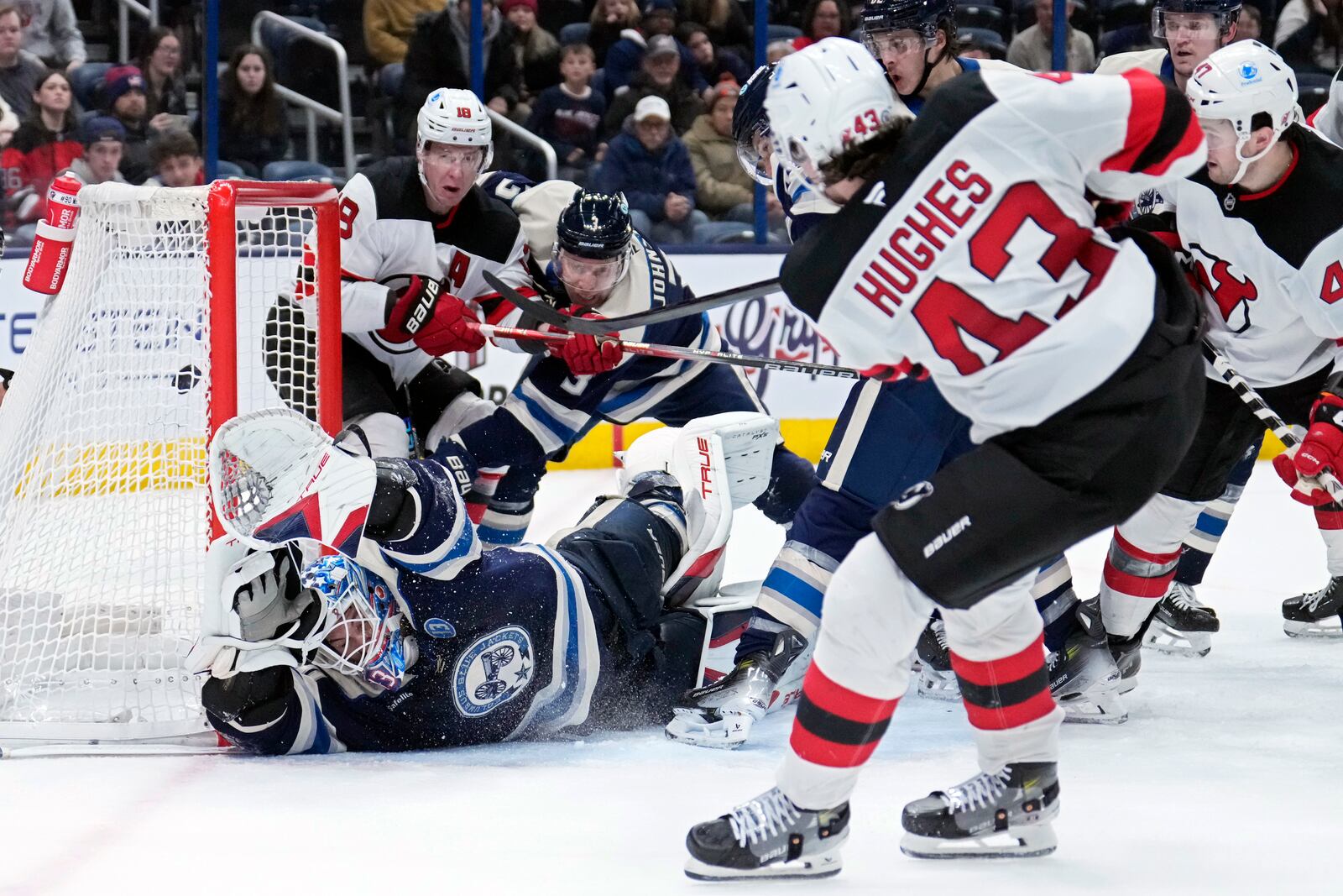 New Jersey Devils defenseman Luke Hughes (43) scores over Columbus Blue Jackets goaltender Elvis Merzlikins, bottom left, in the third period of an NHL hockey game Thursday, Dec. 19, 2024, in Columbus, Ohio. (AP Photo/Sue Ogrocki)