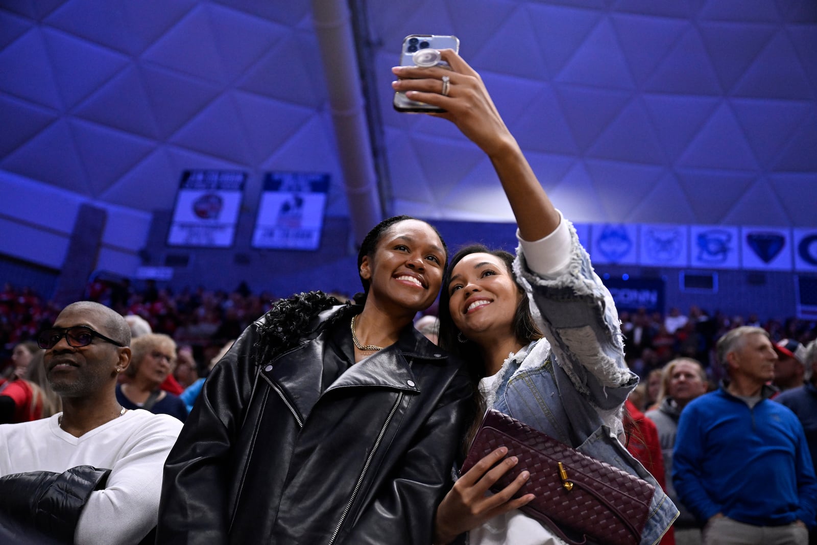 Former UConn players Azura Stevens, left, and Napheesa Collier, right, take a selfie during a pregame ceremony honoring Geno Auriemma and longtime assistant Chris Dailey, Wednesday, Nov. 20, 2024, in Storrs, Conn. (AP Photo/Jessica Hill)