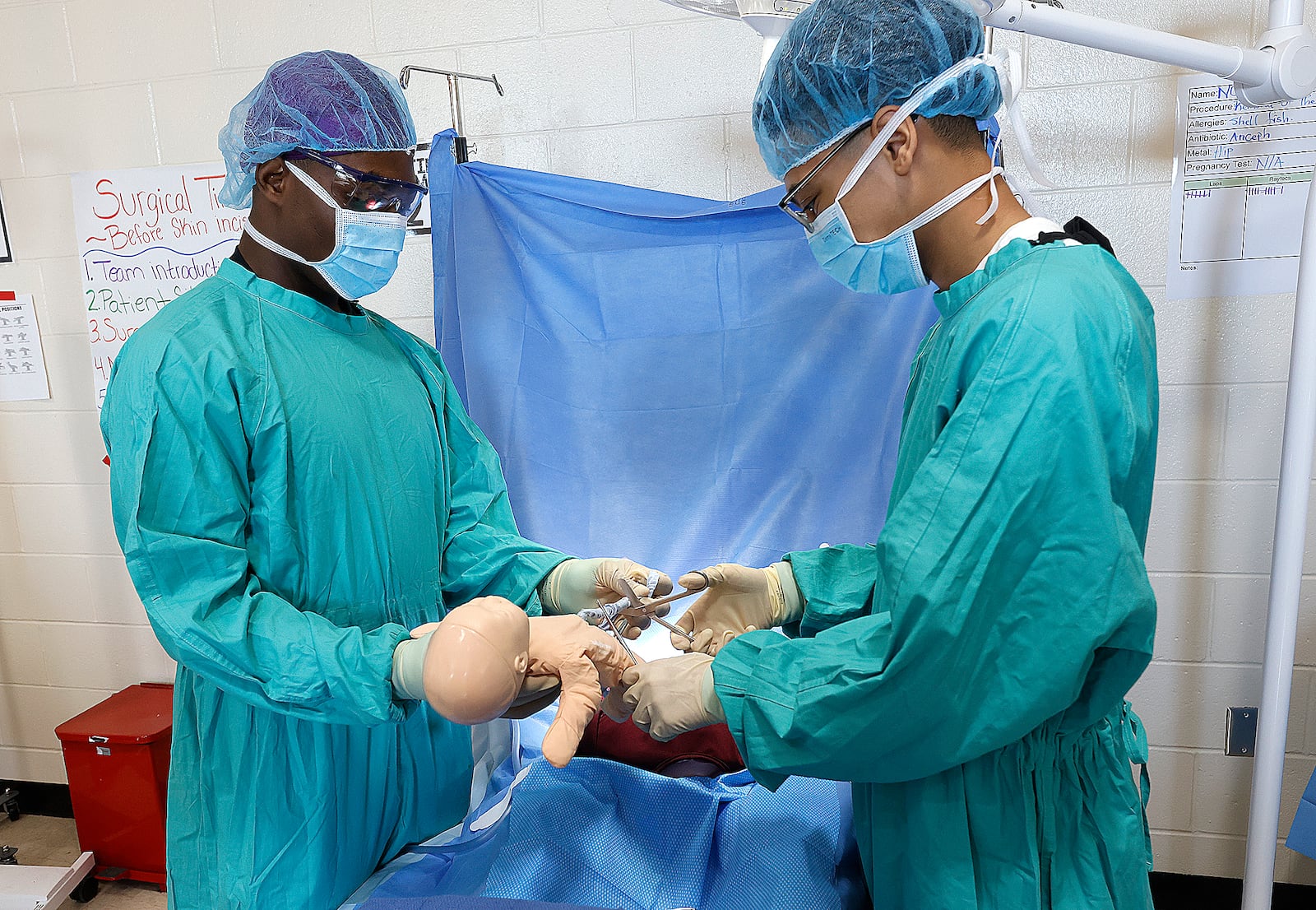 Meadowdale Career Tech Center seniors Oluwatobi Bibilari, left, and Dion Black, right, simulate performing a C-section on a patient during a class on surgical assisting. MARSHALL GORBY\STAFF