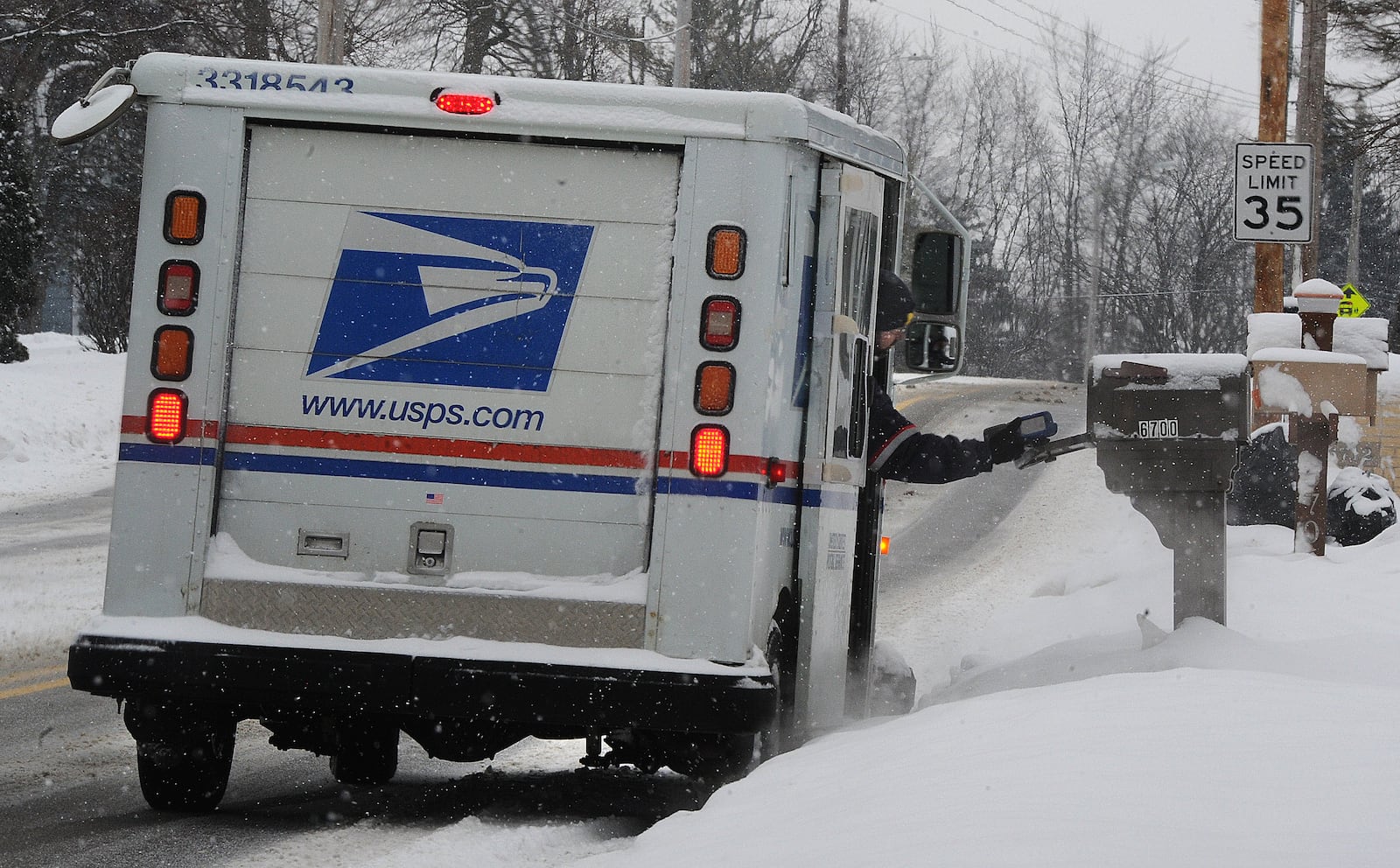 A U.S. Postal Service letter carrier stretches over the snow pack to reach a mailbox on Taylorville Road in Huber Heights Thursday, Feb. 18, 2021. MARSHALL GORBY\STAFF