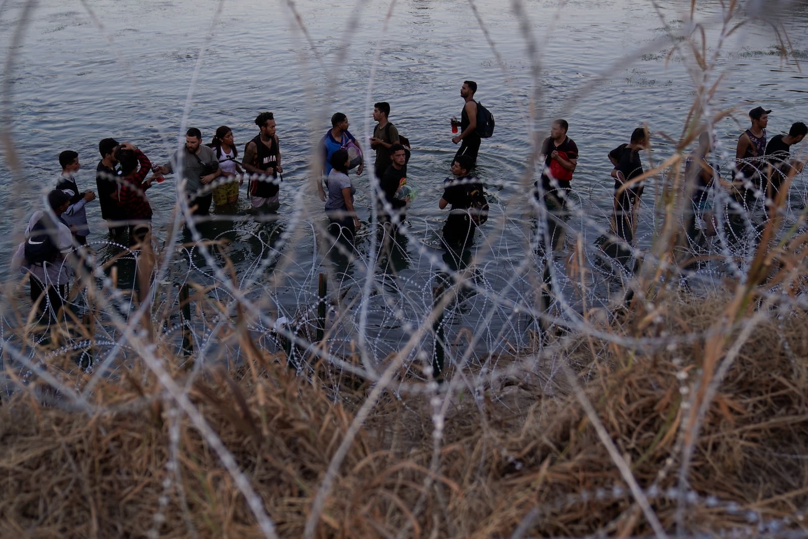 FILE - Migrants wait to climb over concertina wire after they crossed the Rio Grande and entered the U.S. from Mexico on Sept. 23, 2023, in Eagle Pass, Texas. (AP Photo/Eric Gay, File)