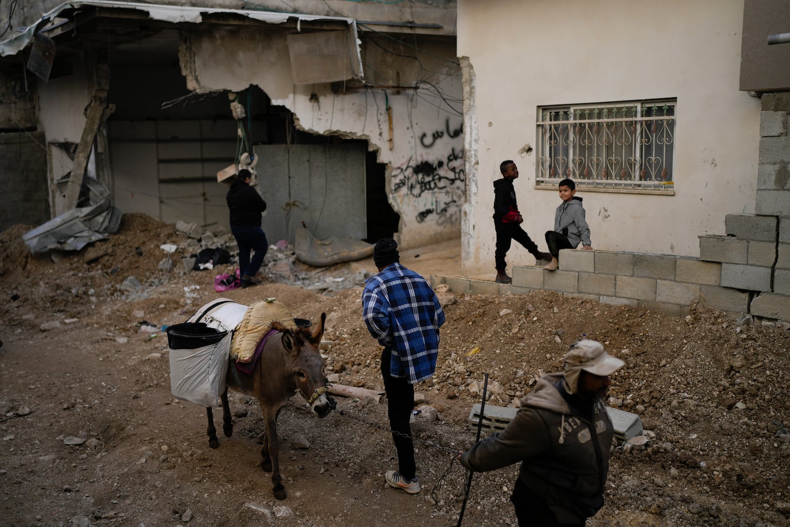 Locals stand next to a damaged building after the latest Israeli military operation, in the West Bank city of Tulkarem, Thursday, Dec. 26, 2024. (AP Photo/Matias Delacroix)