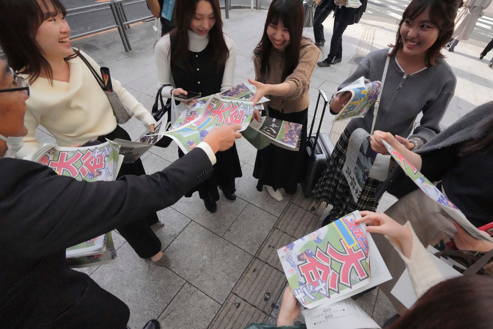 A staff member, left, distributes copies of an extra edition of the Sports Nippon newspaper in Tokyo, Thursday, Oct. 31, 2024, reporting on the Los Angeles Dodgers' victory in the World Series baseball match after the Dodgers defeated the New York Yankees in Game 5 in New York. (AP Photo/Eugene Hoshiko)