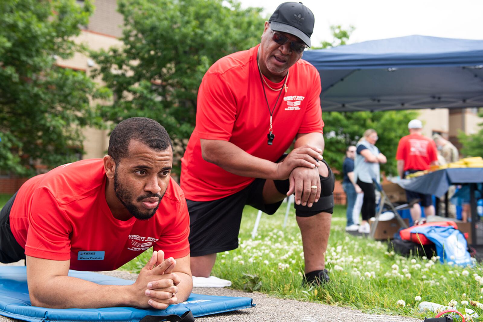 Wesley Prophett, a recreation assistant with the 88th Force Support Squadron, holds a plank while Carl Scott, a group fitness instructor with the 88 FSS, yells out various forms of encouragement during a physical competition as part of the annual Wright-Patterson Air Force Base, Ohio, Fit Fest event, May 27, 2021. During the event people were able to get information about physical and mental health, as well as participate in physical competitions. (U.S. Air Force photo by Wesley Farnsworth)