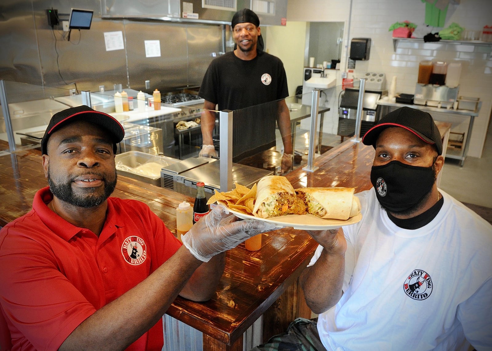 Co-Owners DeShawn Davis, on the left, and Walter Jones, on the right, pose with chief Denyan Blackmon with a King Burrito he made at the new Crazy King Burrito, located at 2624 Colonel Glenn Highway. MARSHALL GORBY\STAFF