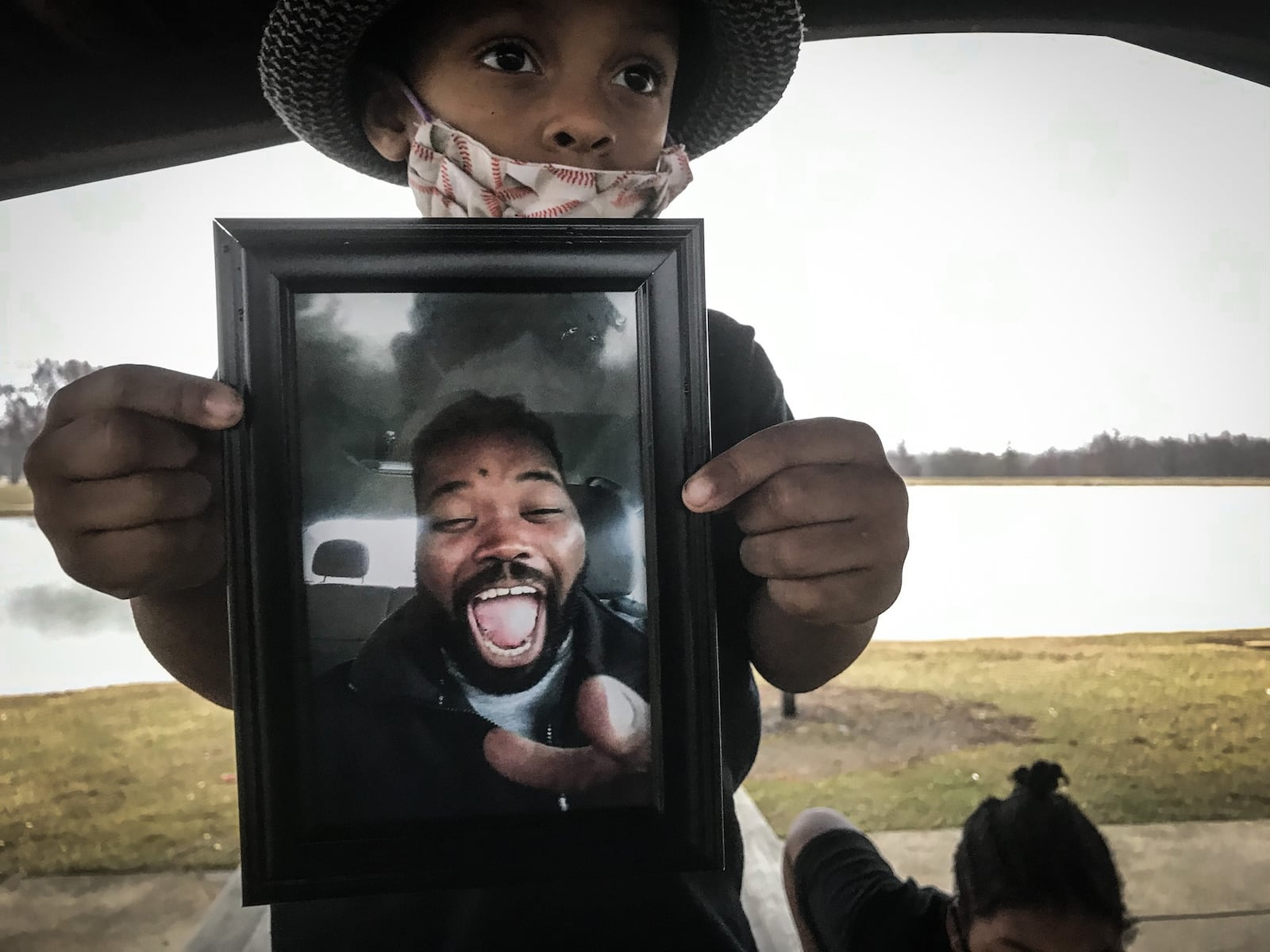 King Cooper holds up a picture of his father, Eberechukwu Cooper who died from COVID-19 in December.