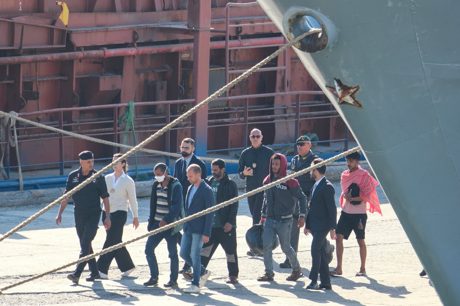 Migrantw and security officials walk at the port of Shengjin, northwestern Albania. Wednesday, Oct. 16, 2024 after disembarking from the Italian navy ship Libra, carrying the first group of 16 migrants intercepted in international waters. (AP Photo/Vlasov Sulaj)