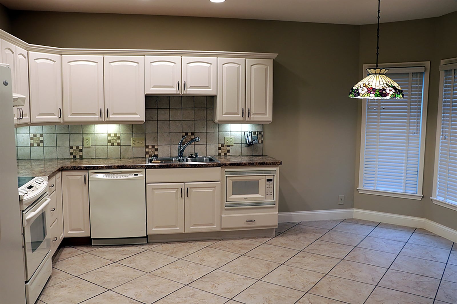 From the lower-level family room is a fully equipped kitchen. White cabinetry with complementing countertops fills two walls and surrounds appliances. The kitchen opens into a bay-like dining area with 3 windows and a glass door that opens to the covered patio and back yard. CONTRIBUTED PHOTO BY KATHY TYLER