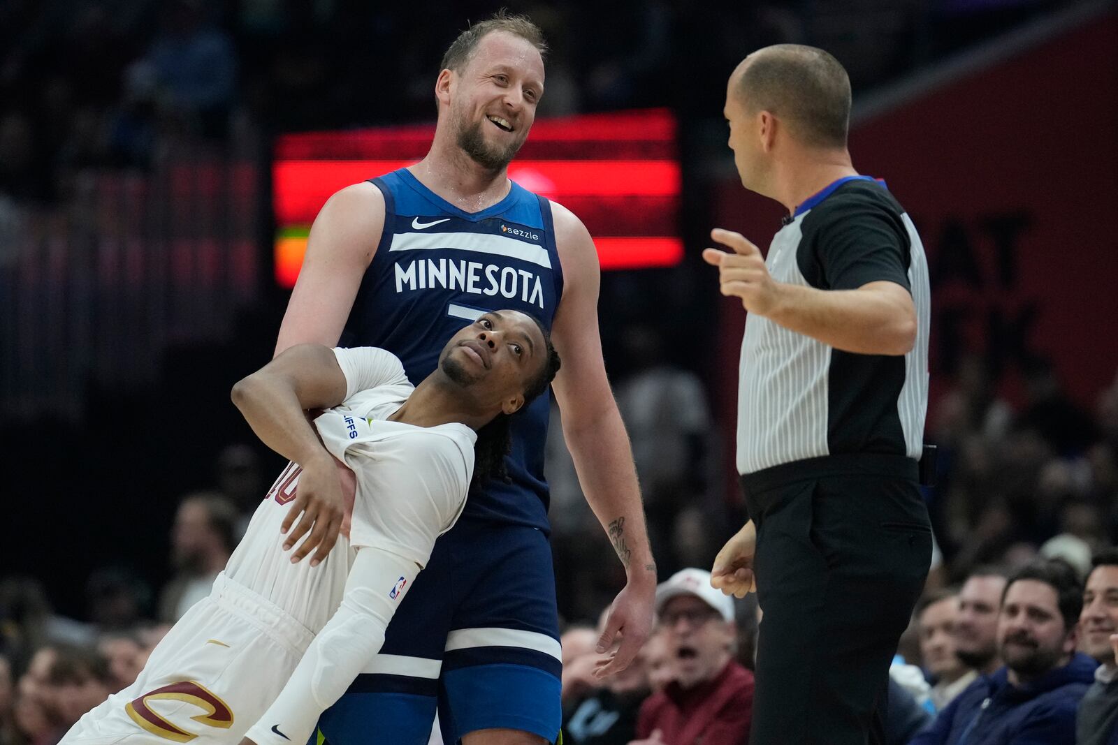 Minnesota Timberwolves guard Joe Ingles, center, clowns around with Cleveland Cavaliers guard Darius Garland, front, as he talks with referee John Goble (10) after a whistle in the first half of an NBA basketball game Monday, Feb. 10, 2025, in Cleveland. (AP Photo/Sue Ogrocki)