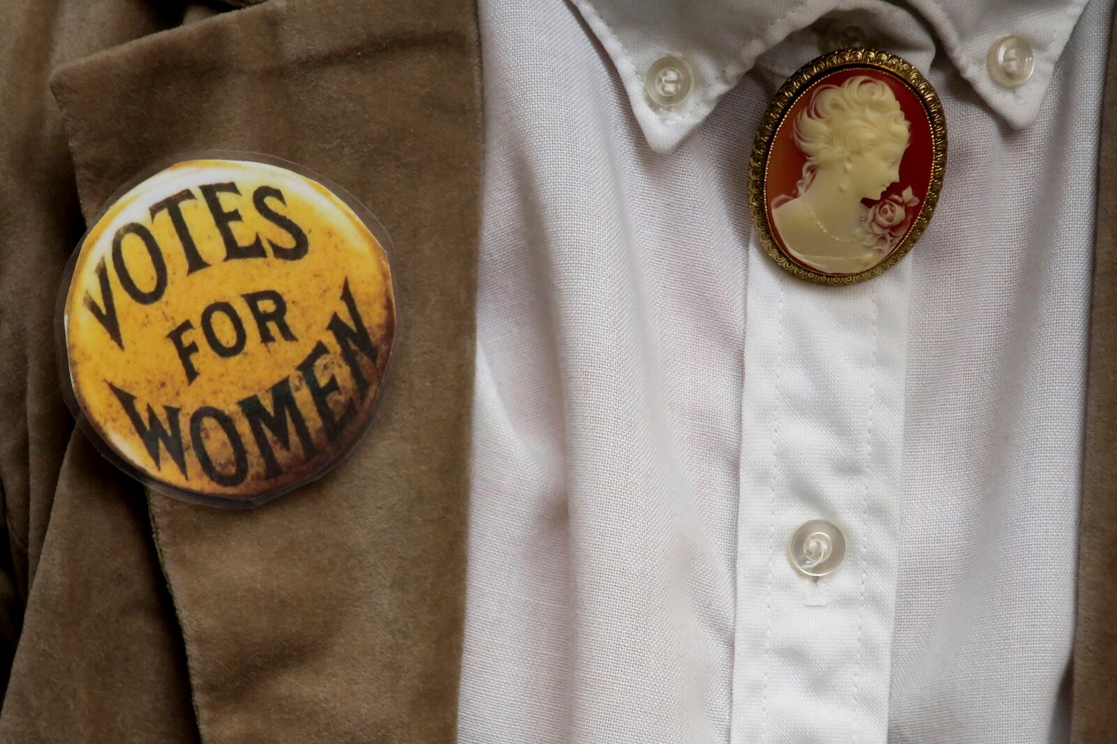 Penny Guy, a retired Topeka, Kansas, middle school teacher who works in the Legislature's documents room at the Statehouse, wears a replica of a 19th Century women's voting rights button as part of a period costume ahead of the unveiling of a mural honoring suffragists, Wednesday, Jan. 29, 2025, in Topeka, Kan. (AP Photo/John Hanna)