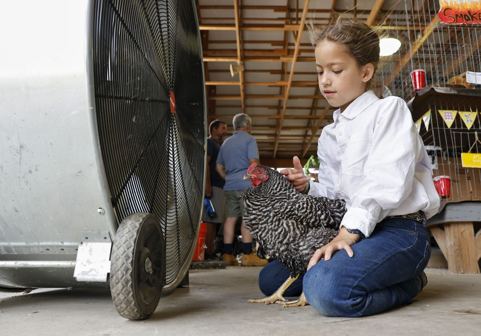 Lydia Peak, 10, cools off in front of a fan with her barred rock chicken, Turkey, during the Warren County Fair Wednesday, July 19, 2023 in Lebanon. NICK GRAHAM/STAFF