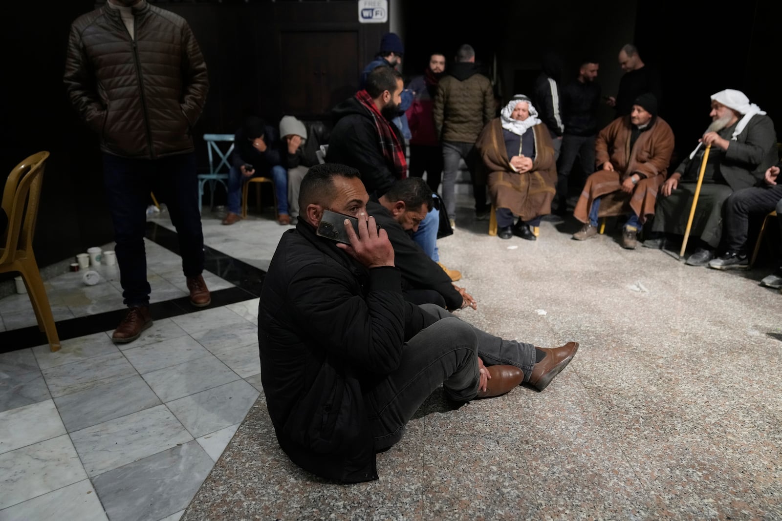 A man waiting for the release of Palestinian prisoners sits on the ground and uses his mobile phone Sunday, Feb. 23, 2025, after receiving news that Israel has delayed the release of hundreds of Palestinian prisoners scheduled for Saturday, in the West Bank city of Ramallah. (AP Photo/Nasser Nasser)