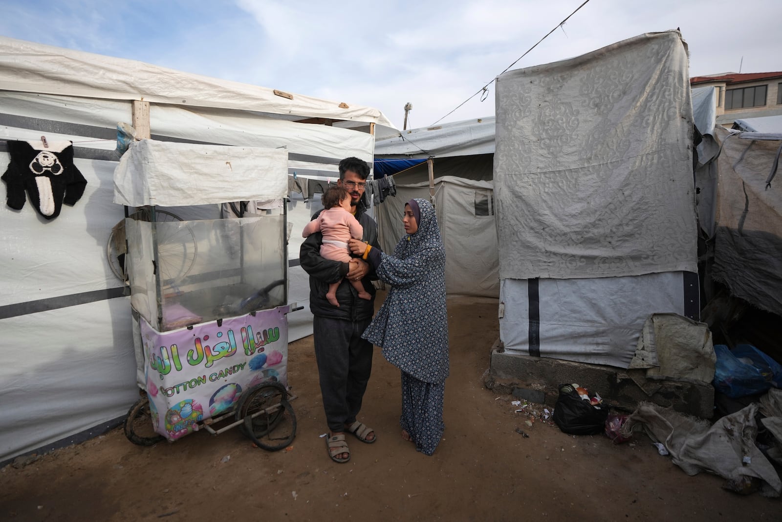 Rola Saqer and her husband Mohammad Zaqout, center, stand with their daughter, Massa Zaqout, who was born on the first day of the war in Gaza, outside of the family tent in Deir al-Balah, Gaza Strip, Tuesday, Jan. 14, 2025. (AP Photo/Abdel Kareem Hana)