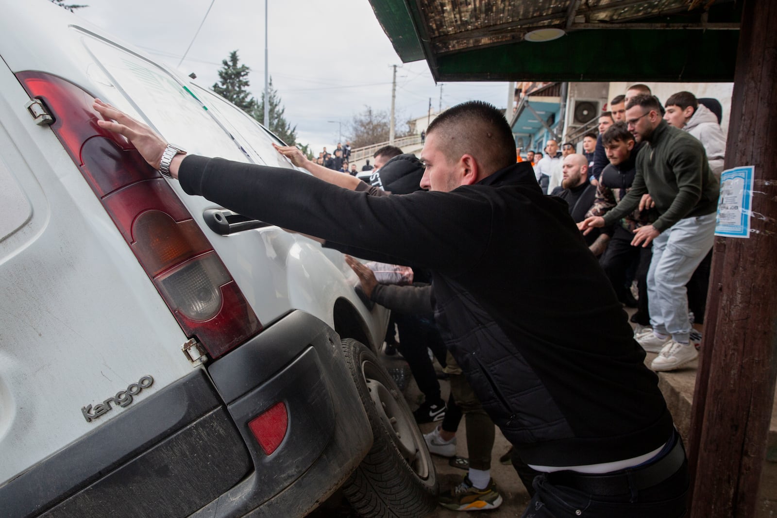 People push a car on its side while protesting near the home of the owner of a nightclub that was the scene of a massive fire, after a vigil for the victims in the town of Kocani, North Macedonia, Monday, March 17, 2025. (AP Photo/Visar Kryeziu)