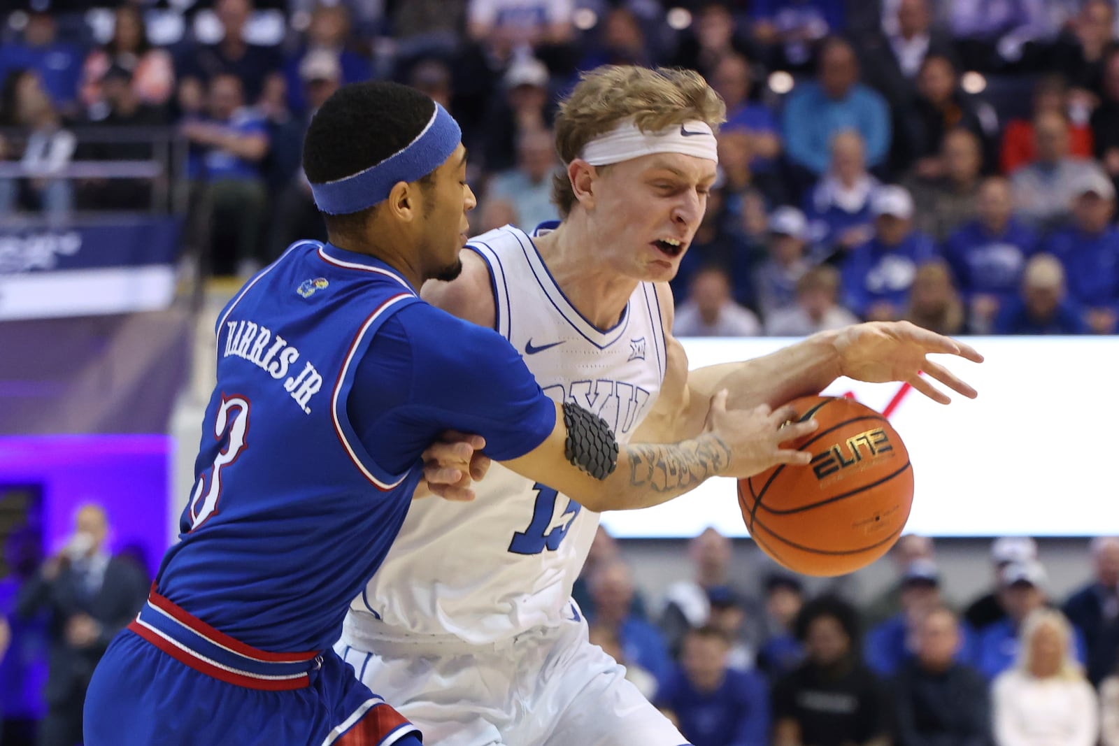 Kansas guard Dajuan Harris Jr. (3) reaches for the ball held by BYU forward Richie Saunders during the first half of an NCAA college basketball game, Tuesday, Feb. 18, 2025, in Provo, Utah. (AP Photo/Rob Gray)