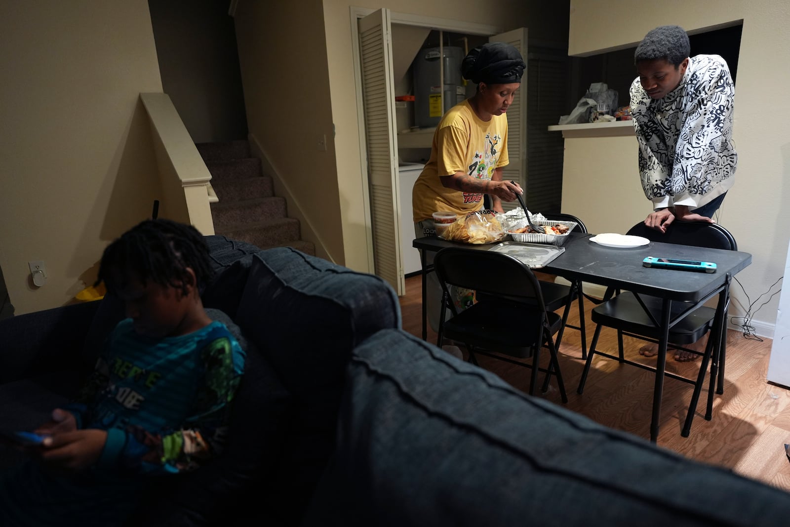 TiAnna Yeldell, center, with her sons Marq'ue, right, and Ivan, left, sets out dinner at her home, Thursday, Nov. 14, 2024, in Missouri City, Texas. (AP Photo/Eric Gay)