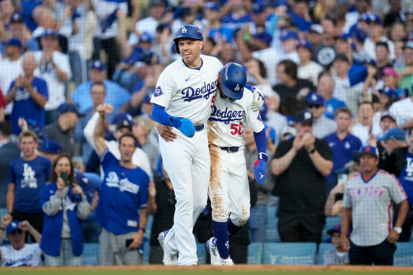 Los Angeles Dodgers' Freddie Freeman, left, and Mookie Betts celebrate after they scored on a single by Max Muncy during the first inning in Game 1 of a baseball NL Championship Series against the New York Mets, Sunday, Oct. 13, 2024, in Los Angeles. (AP Photo/Ashley Landis)