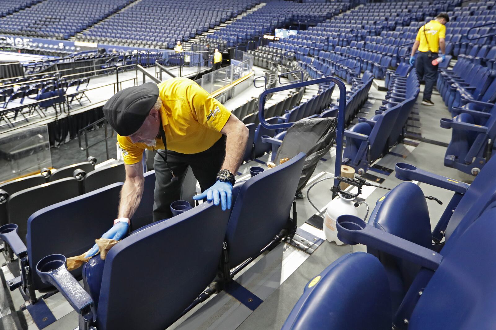 FILE - Luis Rivera, left, sanitizes seats at the Bridgestone Arena after the remaining NCAA college basketball games in the Southeastern Conference tournament were canceled due to coronavirus concerns, Thursday, March 12, 2020, in Nashville, Tenn. (AP Photo/Mark Humphrey, File(