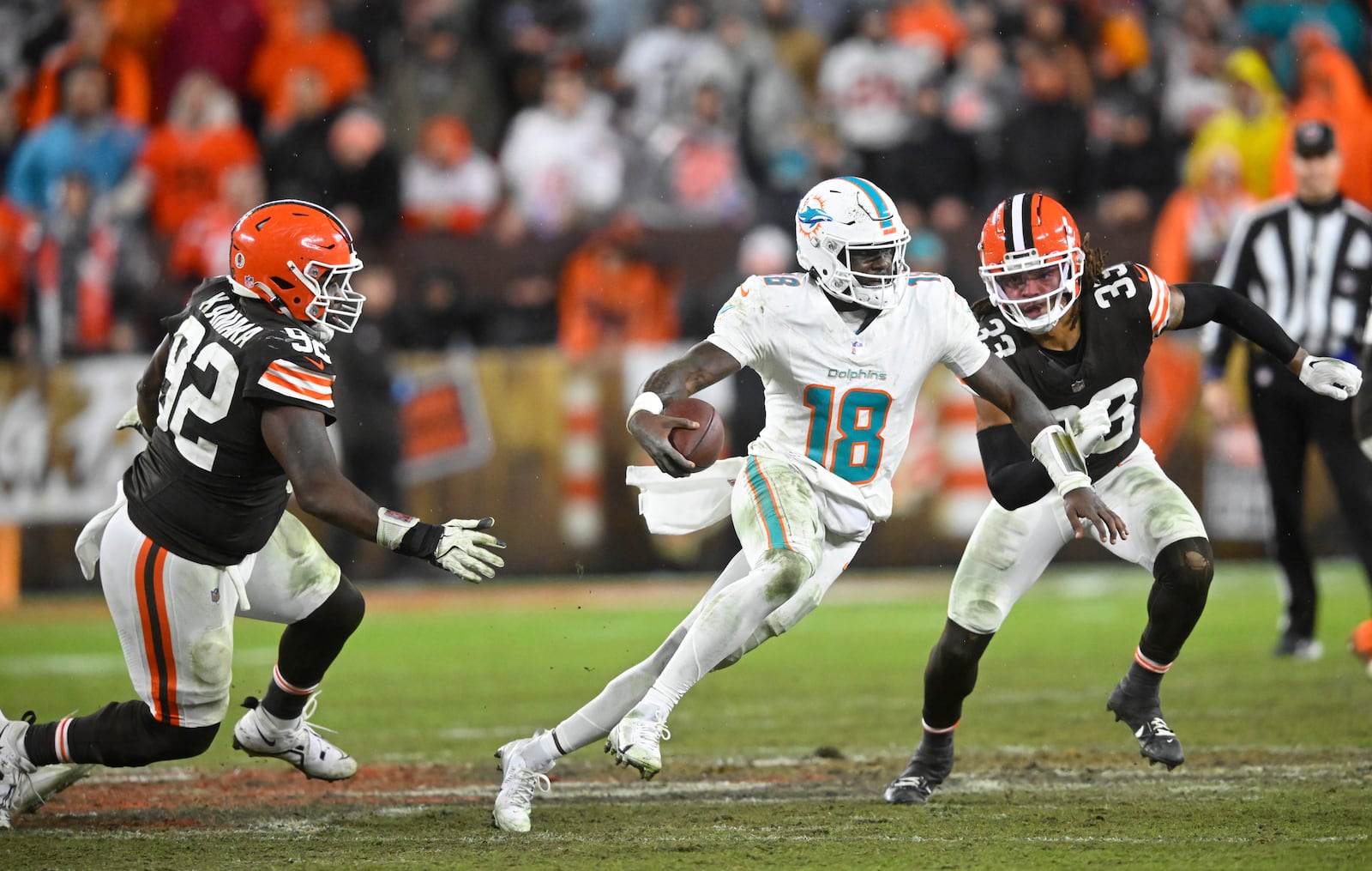 Miami Dolphins quarterback Tyler Huntley (18) scrambles for a first down as Cleveland Browns defensive end Sam Kamara (92) and safety Ronnie Hickman (33) defend during the second half of an NFL football game Sunday, Dec. 29, 2024, in Cleveland. (AP Photo/David Richard)