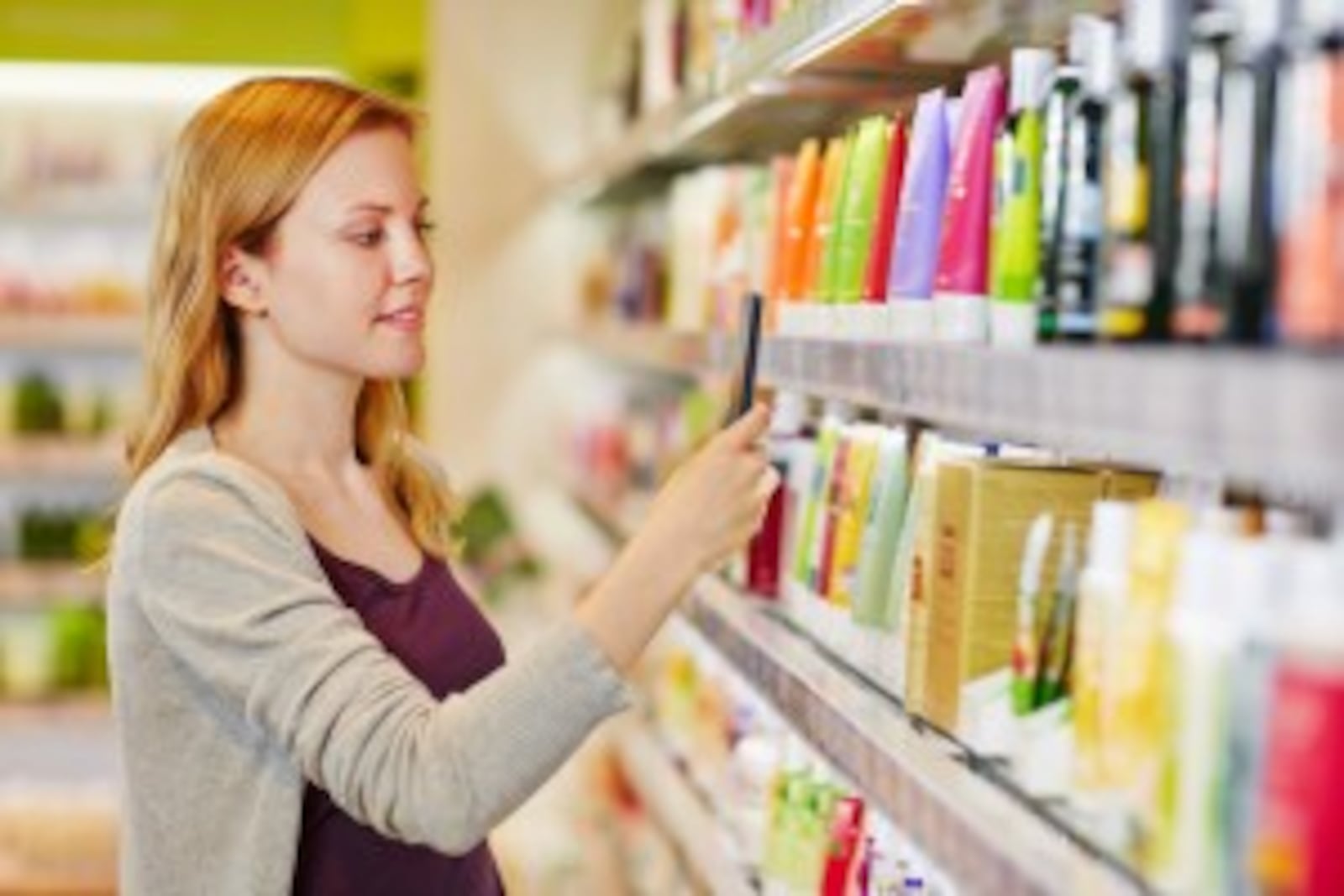 Young woman comparing prices with a smartphone app in a drugstore