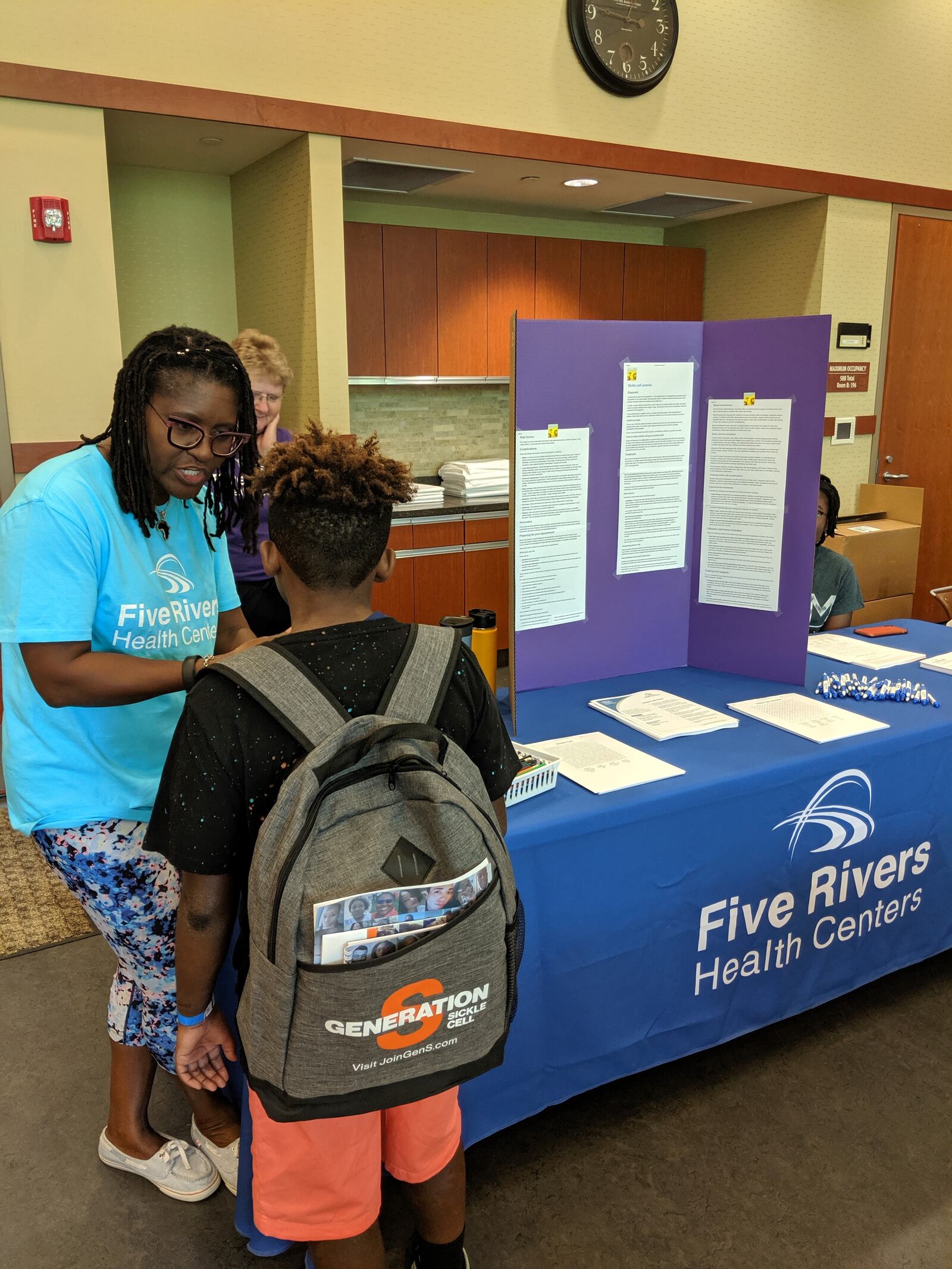 Dr. Anim speaking with a young sickle-cell anemia patient at an event.