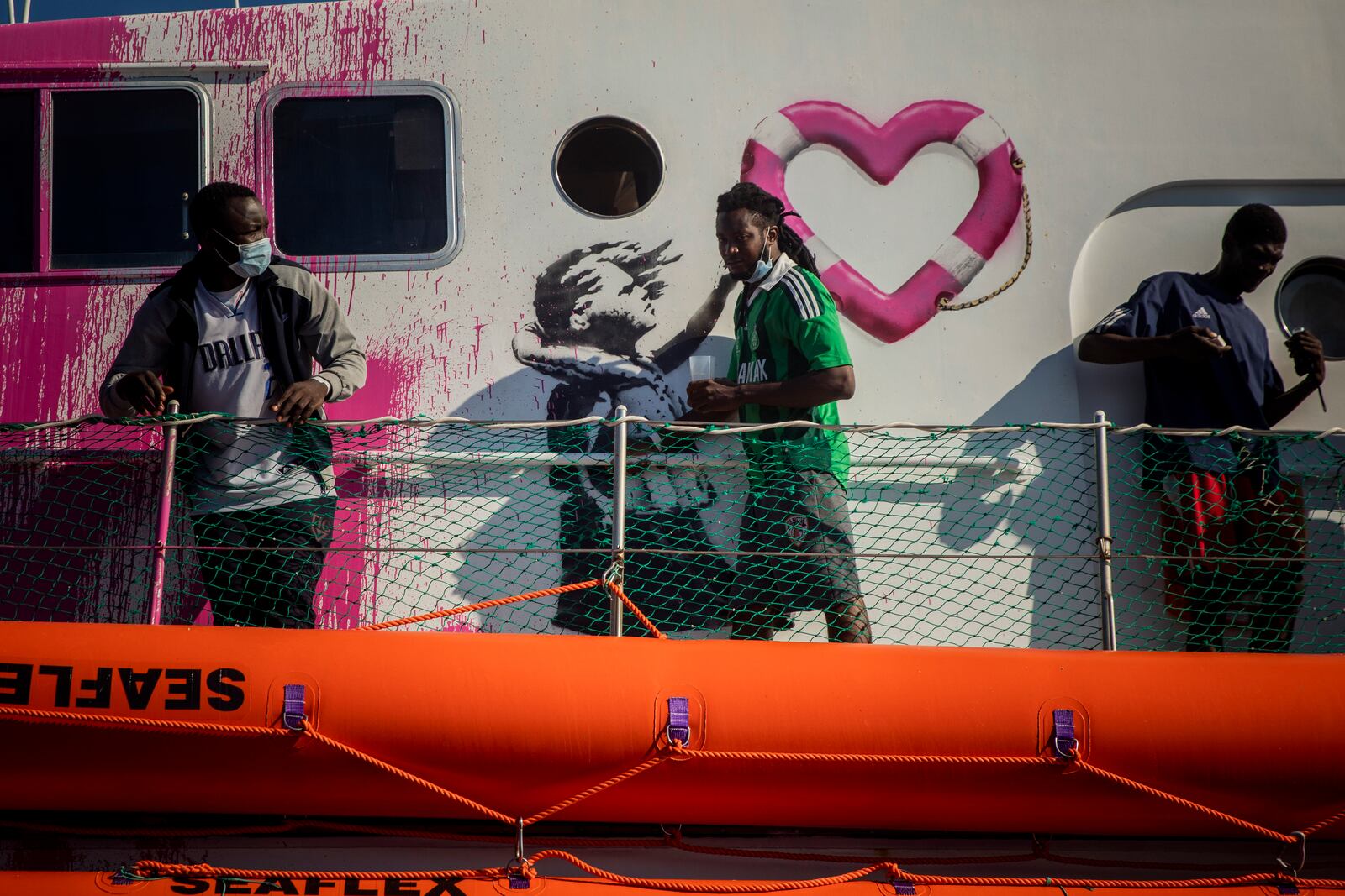 A man walks past a painting by British artist Banksy on the deck of the Louise Michele rescue vessel, after performing 2 rescue operations on the high seas in the past days, 70 miles south west Malta, Central Mediterranean sea, Saturday, Aug. 29, 2020. A rescue ship painted and sponsored by British artist Banksy saved another 130 migrants stranded on a rubber boat in the Southern Mediterranean Sea. (AP Photo/Santi Palacios)