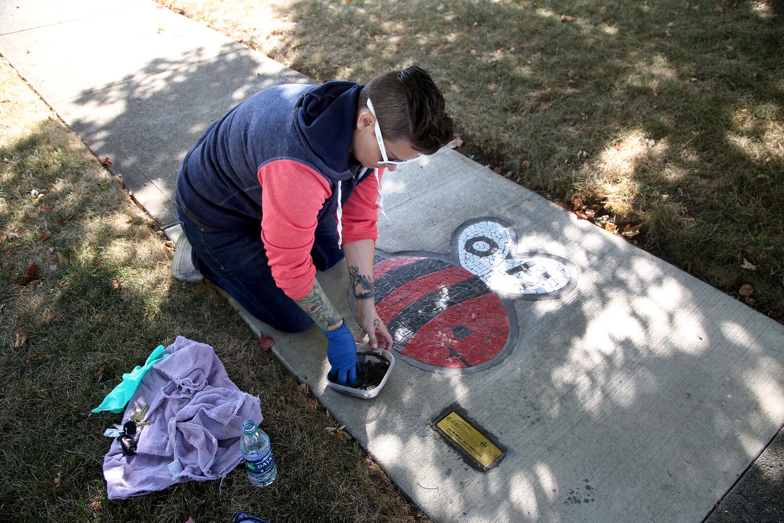 Jes McMillan, founder of The Mosaic Institute of Greater Dayton, works on a mosaic bumble bee in Kettering's Haverstick neighborhood. The piece is a part of a larger neighborhood artwork called "Bee Ambitious," which incorporates a word scramble and games. LISA POWELL / STAFF