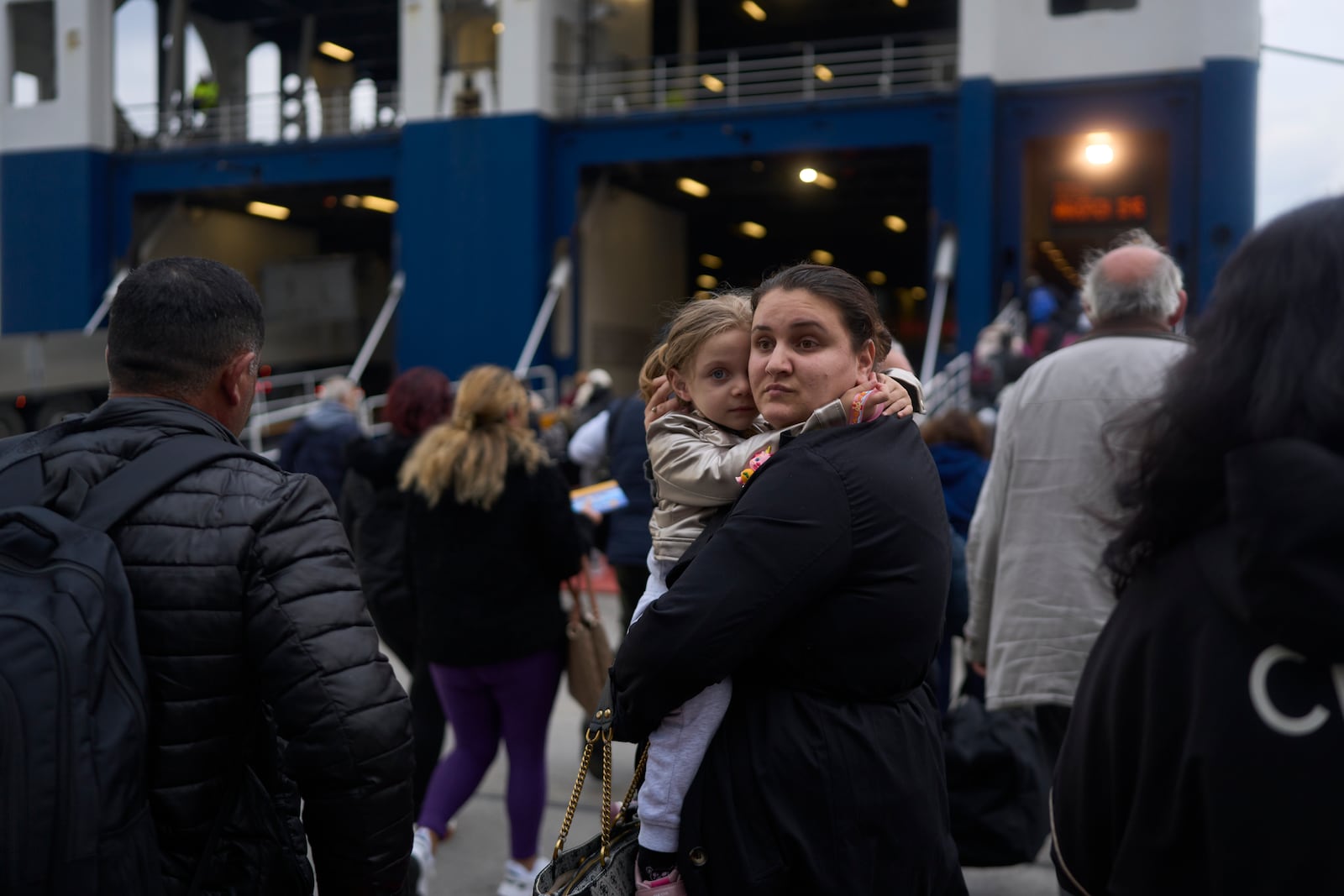 A woman with her child prepare to board a ferry bound for the Greek mainland, in the earthquake-struck island of Santorini, Greece, Tuesday, Feb. 4, 2025. (AP Photo/Petros Giannakouris)