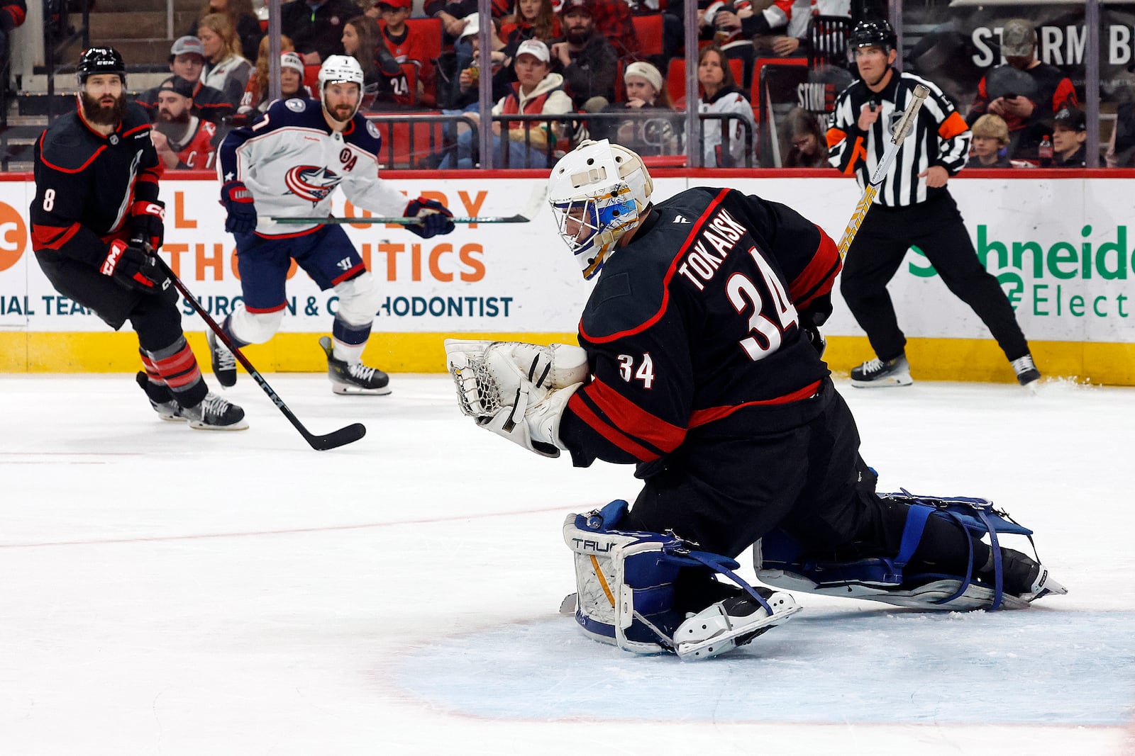 Carolina Hurricanes goaltender Dustin Tokarski (34) gloves a shot from Columbus Blue Jackets' Sean Kuraly (7) with Brent Burns (8) nearby during the first period of an NHL hockey game in Raleigh, N.C., Sunday, Dec. 15, 2024. (AP Photo/Karl B DeBlaker)