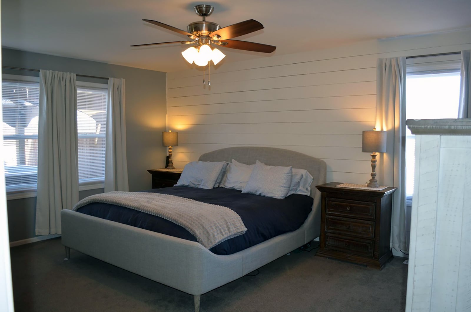 The primary bedroom suite has a shiplap accent wall, neutral carpeting and a ceiling fan.