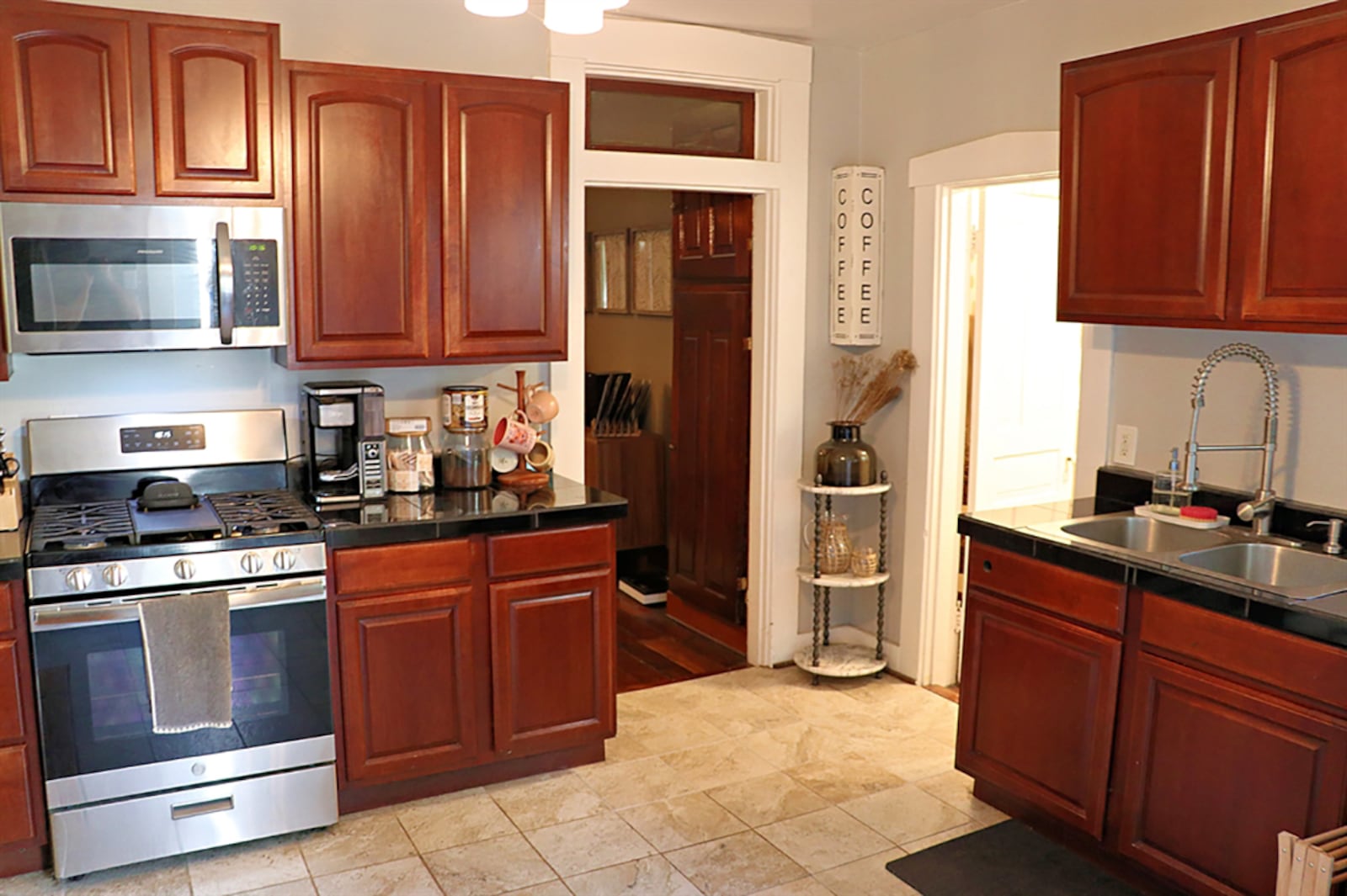 Ceramic-tile flooring fills most of the kitchen with the exception of the wooden cellar door. There is space near a side window for a breakfast table. Two walls are filled with cherry cabinetry and dark granite countertops. A double sink is along one wall and the stainless-steel appliances are along the other wall. CONTRIBUTED PHOTO BY KATHY TYLER