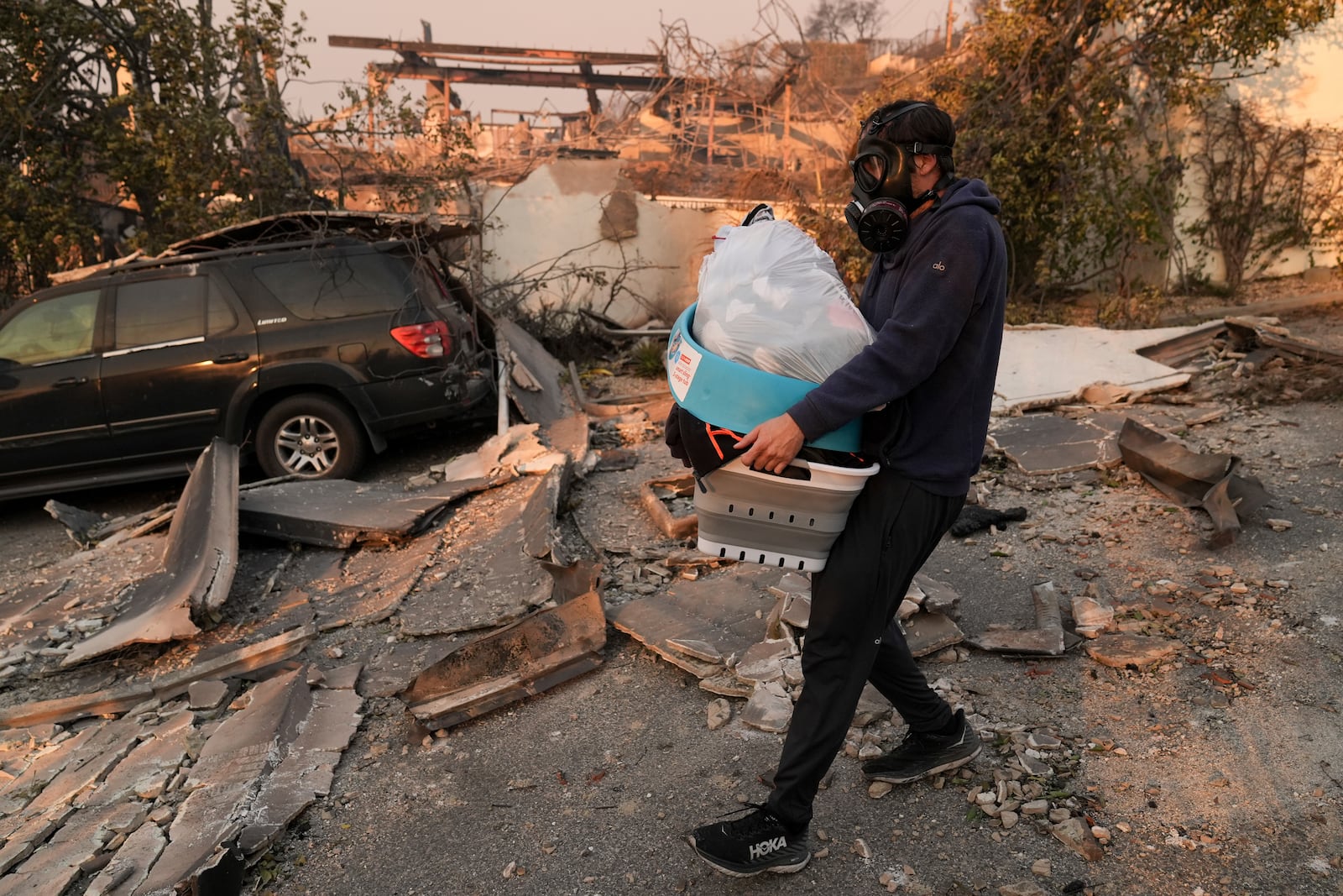 Josh Lederer wears a mask to protect him from fumes as he retrieves his children's clothes from his fire-raved property in the aftermath of the Palisades Fire in the Pacific Palisades neighborhood of Los Angeles, Thursday, Jan. 9, 2025. (AP Photo/Jae C. Hong)