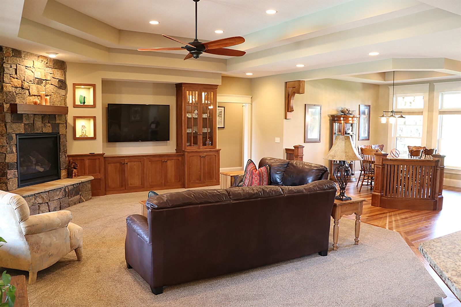 A double tray ceiling is above the great room. Rustic stone surrounds the gas fireplace, which has a raised stone hearth. Shaker-style cabinets are built-in along one wall as well as lighted display cases with glass doors. Triple windows with transoms and wide wood molding look out over the sun patio and pool deck. CONTRIBUTED PHOTO BY KATHY TYLER