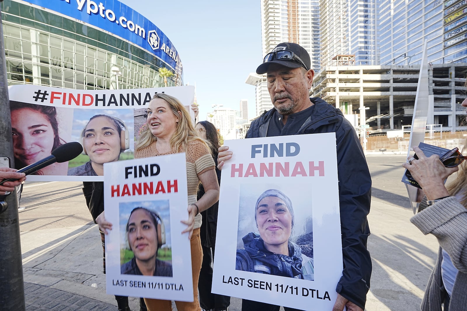 Ryan Kobayashi, right, holds a picture of his missing daughter Hannah Kobayashi outside Crypto.com Arena, Thursday, Nov. 21, 2024 in Los Angeles. (AP Photo/Damian Dovarganes)