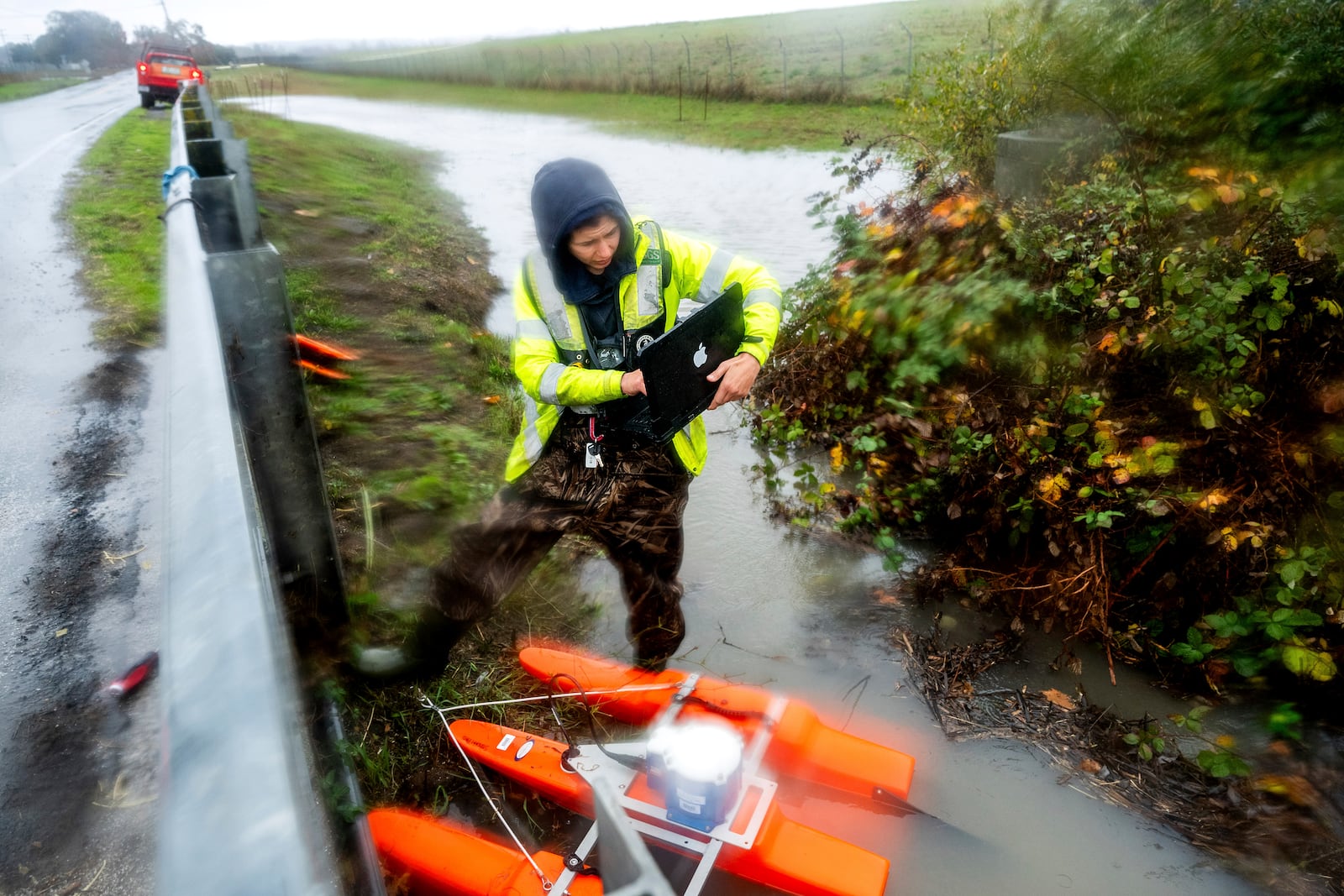 U.S. Geological Survey Hydrologic technician Isabella Karamitsos works to deploy a sensor to measure water flow as heavy rains impact Santa Rosa, Calif., on Wednesday, Nov. 20, 2024, (AP Photo/Noah Berger)