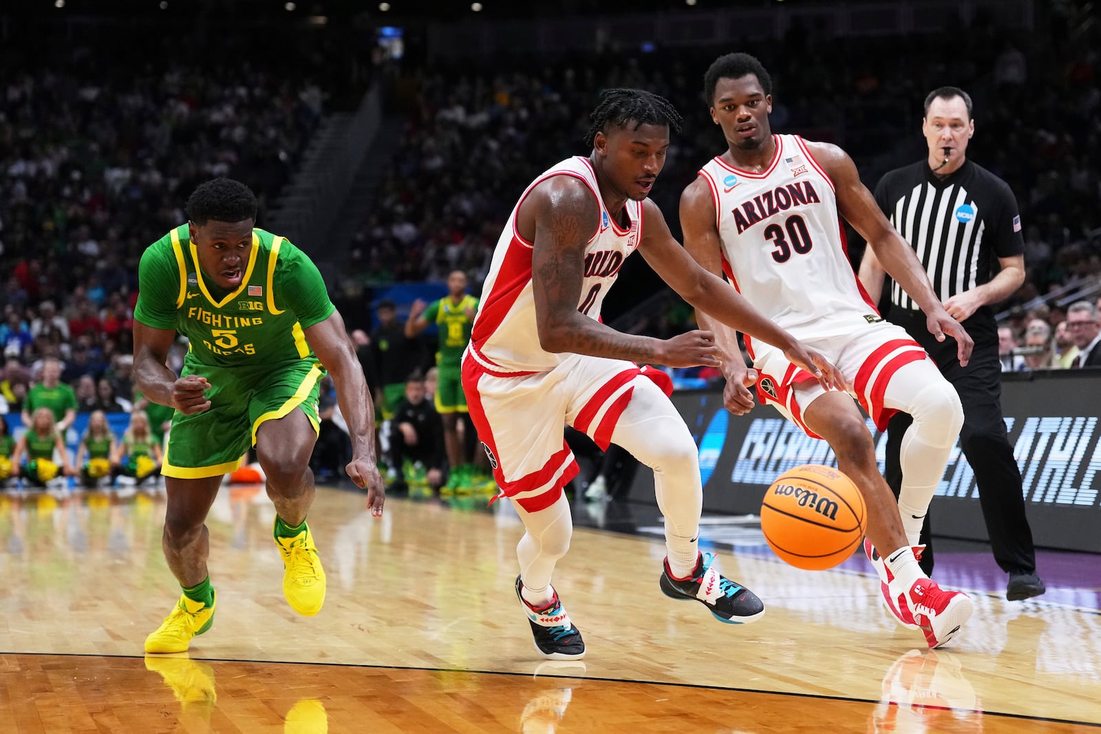 Arizona guard Jaden Bradley (0) grabs the loose ball as teammate Tobe Awaka (30) looks on against Oregon guard TJ Bamba, left, during the first half in the second round of the NCAA college basketball tournament, Sunday, March 23, 2025 in Seattle. (AP Photo/Lindsey Wasson)