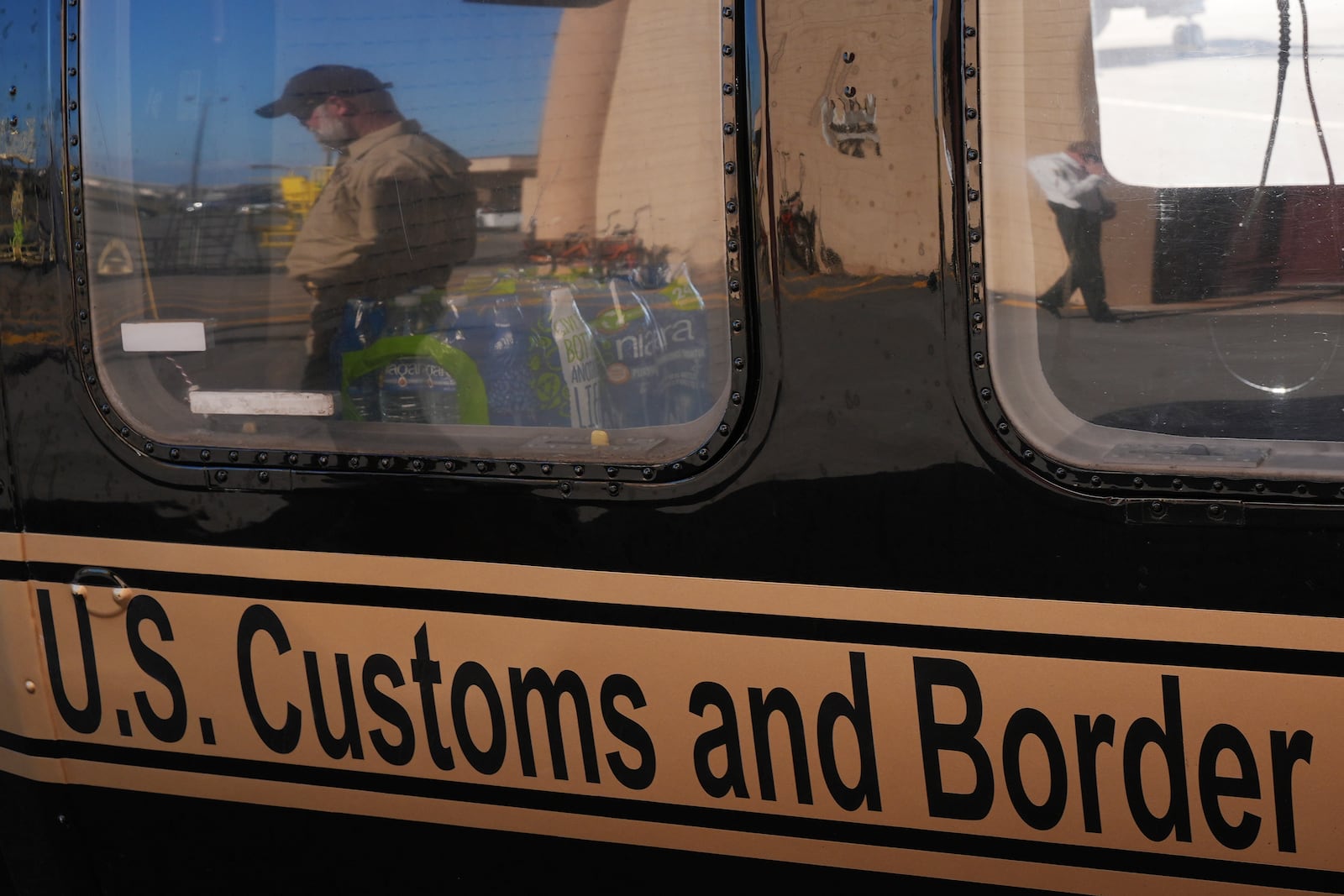 A U.S. Customs and Border Protection agent walking past is reflected in the window of a helicopter at Homestead Air Force Base ahead of a press conference by Florida Gov. Ron DeSantis, Wednesday, Feb. 26, 2025, in Homestead, Fla. (AP Photo/Rebecca Blackwell)