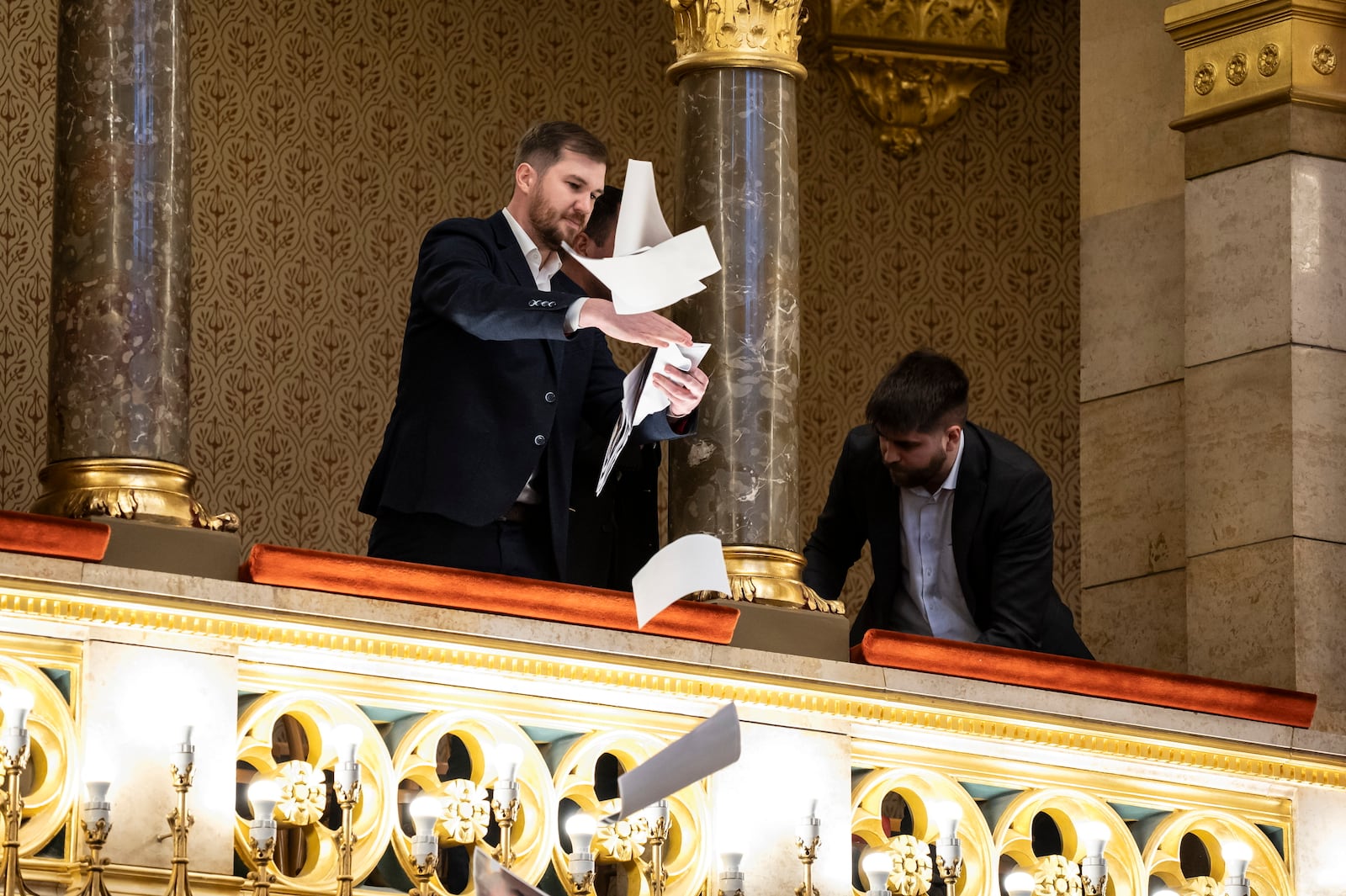 Ferenc Gelencser of Momentum, left, throws pamphlets from the balcony during the plenary session of the Hungarian parliament in Budapest, Hungary, Tuesday, March 18, 2025. (Boglarka Bodnar/MTI via AP)