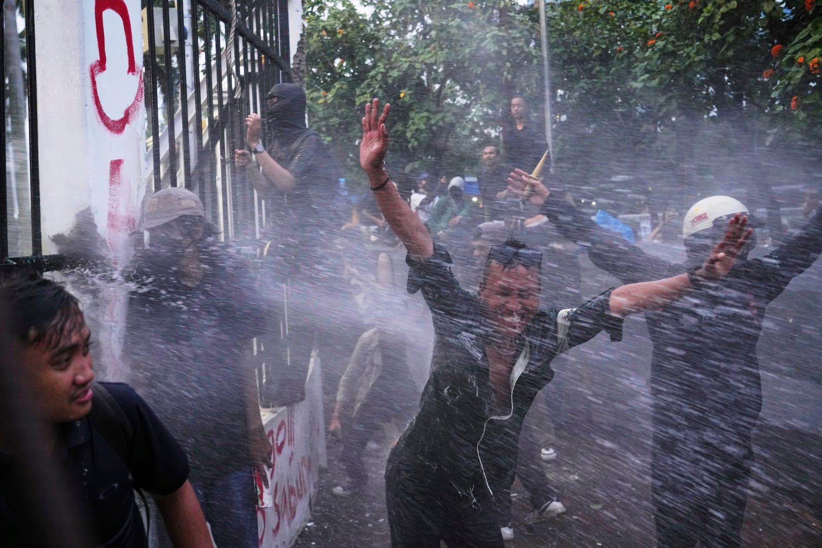 Protesters react as police use a water cannon during a rally in Jakarta, Indonesia, Thursday, March 20, 2025, against the passing of a controversial revision of a military law that will allow military officers to serve in more government posts without resigning from the armed forces. (AP Photo/Tatan Syuflana)