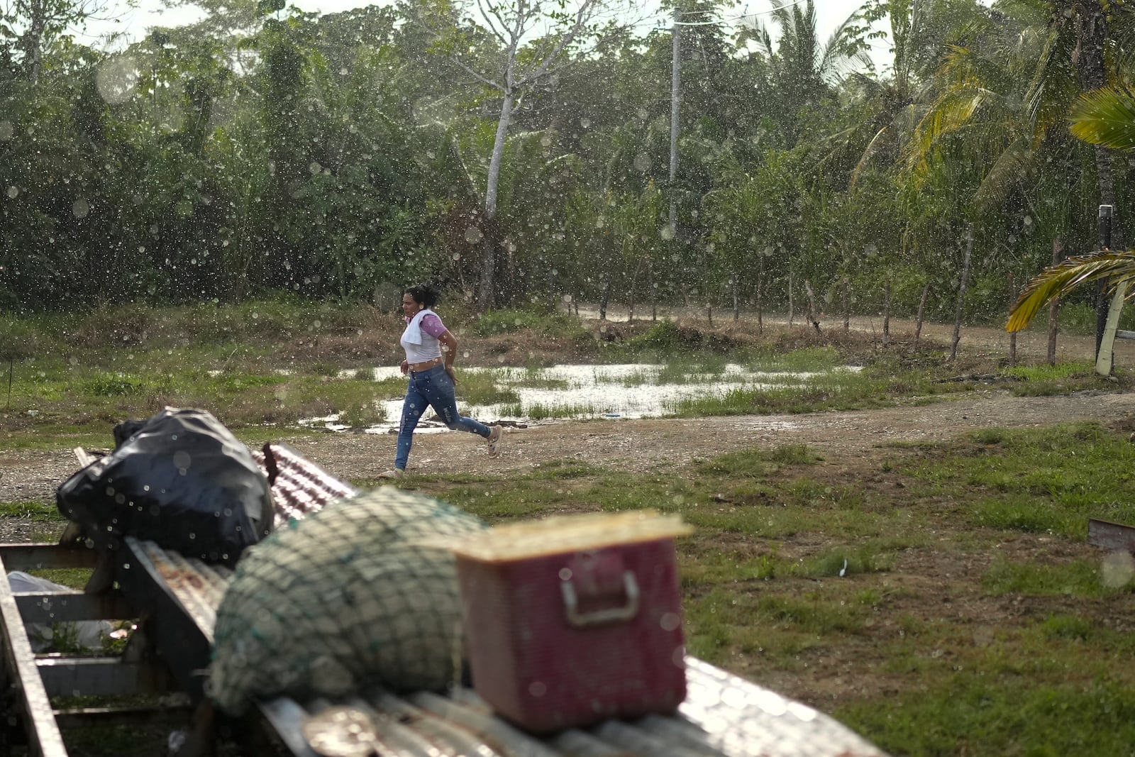 A Venezuelan migrant runs for cover from the rain at the house where she is camping in Puerto Carti, on Panama's Caribbean coast, Saturday, Feb. 22, 2025, where she plans to board a boat to Colombia after turning back from southern Mexico where they gave up hopes of reaching the U.S. amid President Trump's crackdown on migration. (AP Photo/Matias Delacroix)