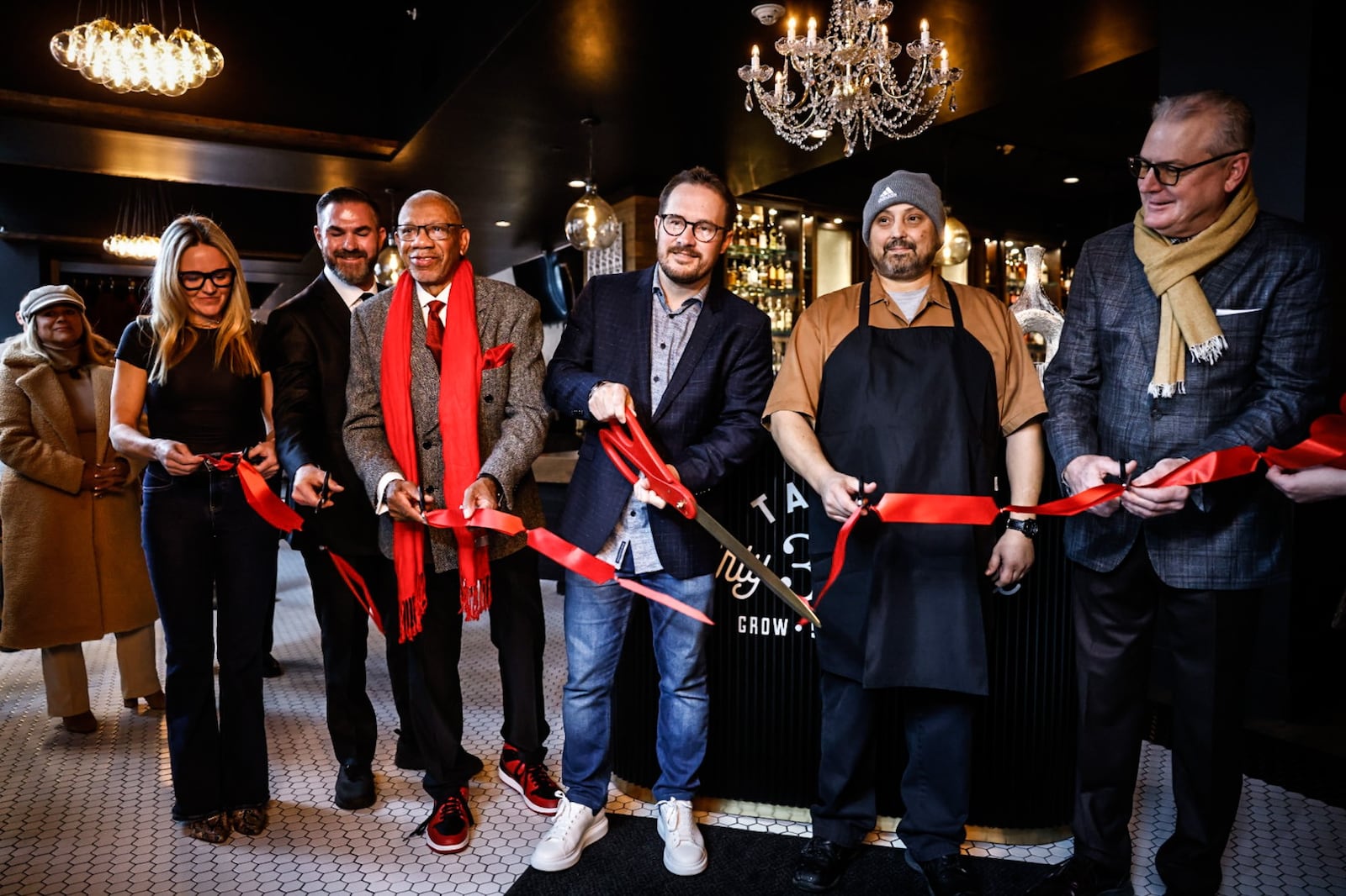 Table 33 owner Charlie Carroll, center with scissors, cuts the ribbon to open his restaurant at the Dayton Arcade on Friday, Dec. 13, 2024. Table 33 was originally planning to open in the Arcade’s Kuhns Building at the corner of Fourth and Main streets, but was able to shift its restaurant development to the former space of Est! Est!! Est!!! when that restaurant closed in July. The new 5,800-square-foot space features several different dining areas. JIM NOELKER/STAFF