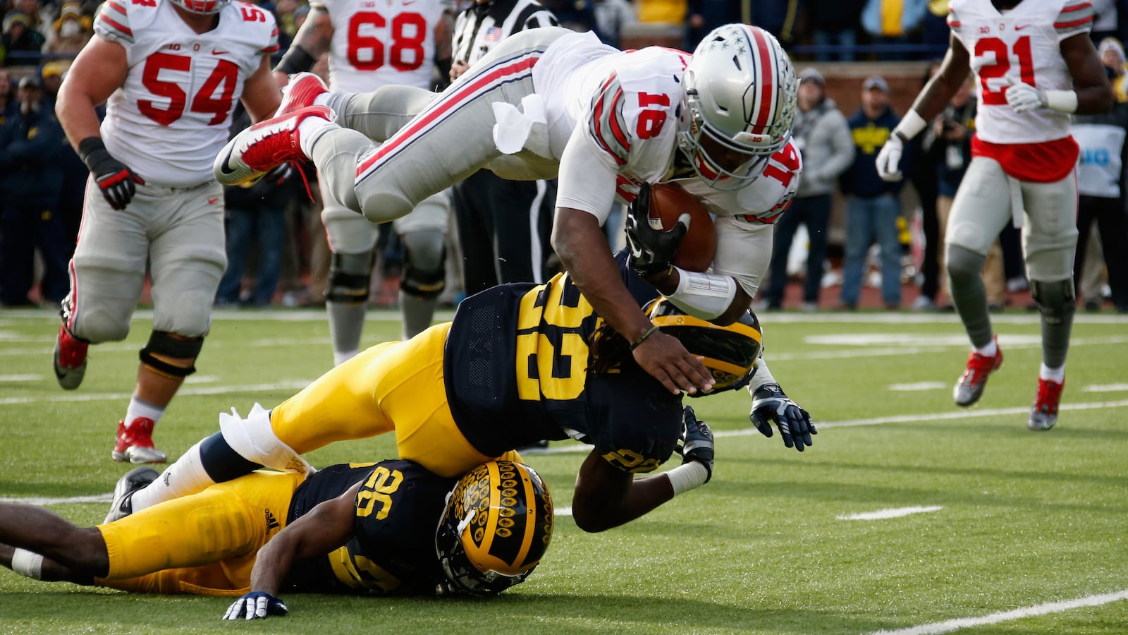 ANN ARBOR, MI - NOVEMBER 28:  Quarterback J.T. Barrett #16 of the Ohio State Buckeyes dives over Jarrod Wilson #22 and Jourdan Lewis #26 of the Michigan Wolverines for a third quarter touchdown at Michigan Stadium on November 28, 2015 in Ann Arbor, Michigan.  (Photo by Gregory Shamus/Getty Images)