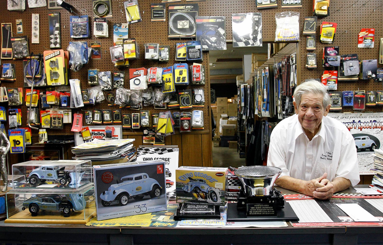 "Ohio George" Montgomery leans on the counter at his speed shop in Dayton. On the left are model car kits of his 1933 Willys Gasser. Contributed photograph by Skip Peterson