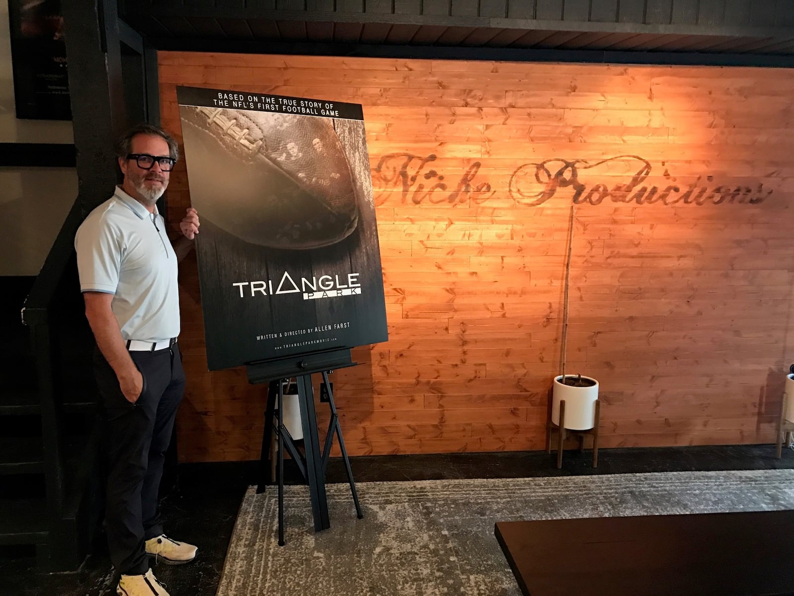 Local filmmaker Allen Farst at his Niche Production headquarters in Centerville with a poster for his upcoming documentary, “Triangle Park,”  and the NFL’s first-ever game, played right here in Dayton by the Dayton Triangles and the Columbus Panhandles at Triangle Park in 1920. Tom Archdeacon/STAFF